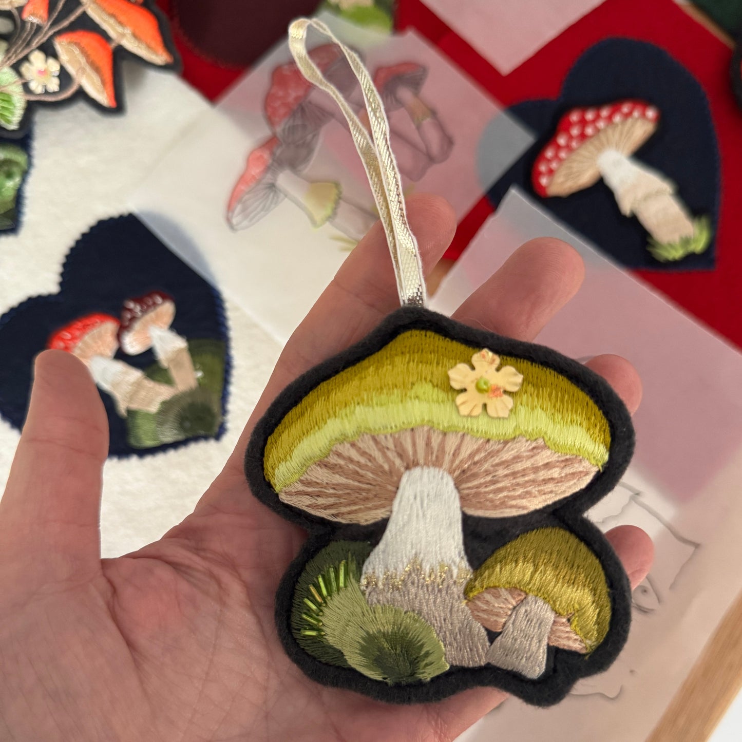 Embroidered mushroom patch held in a hand with embroidered patches in the background