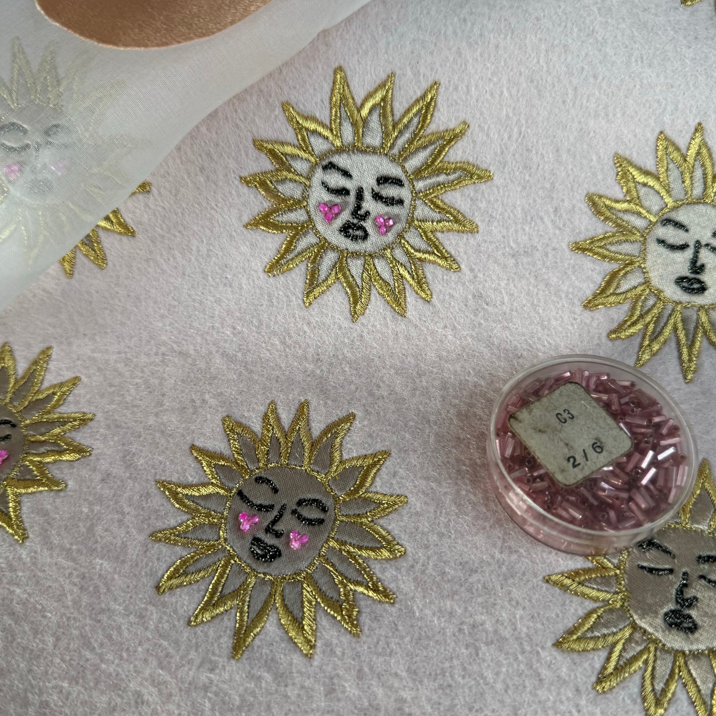 A close-up of a few un-cut suns, shown lying flat with a small clear round pot of pink beads sat on top