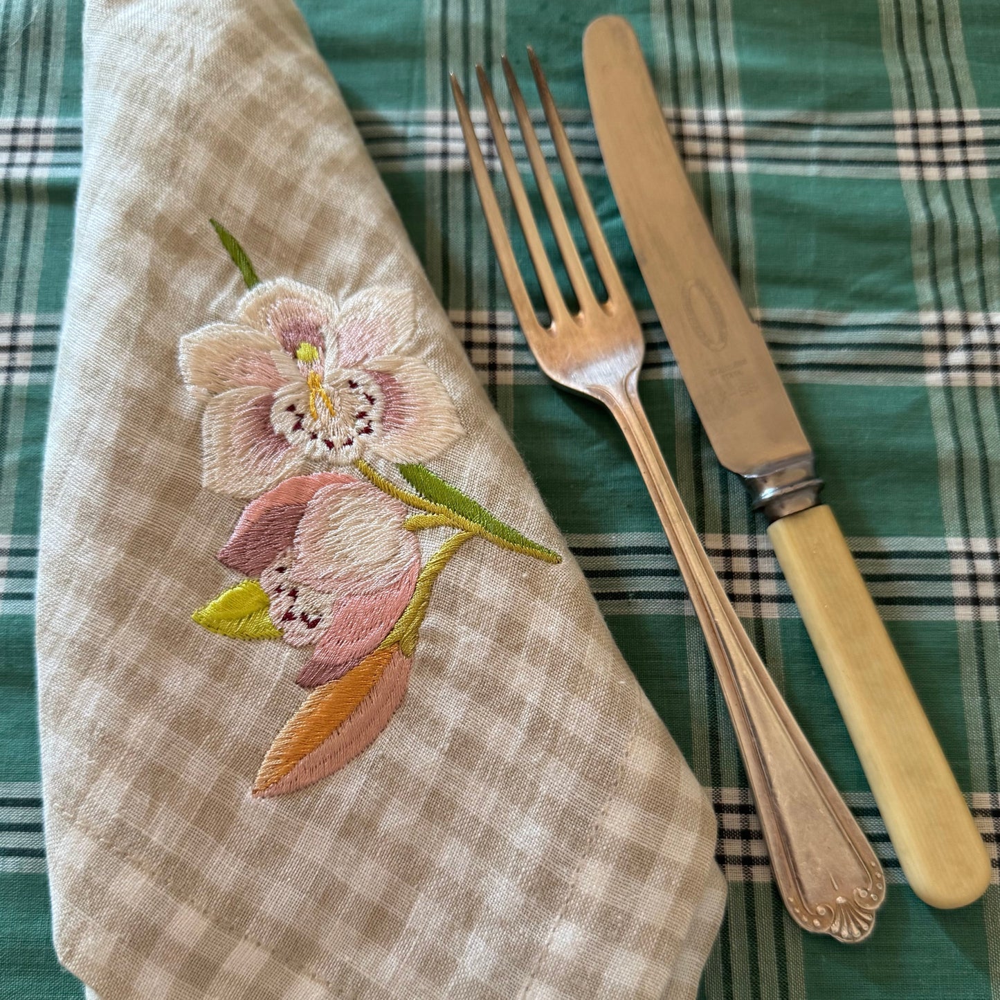 Embroidered orchid on napkin with a fork and knife on a plaid tablecloth