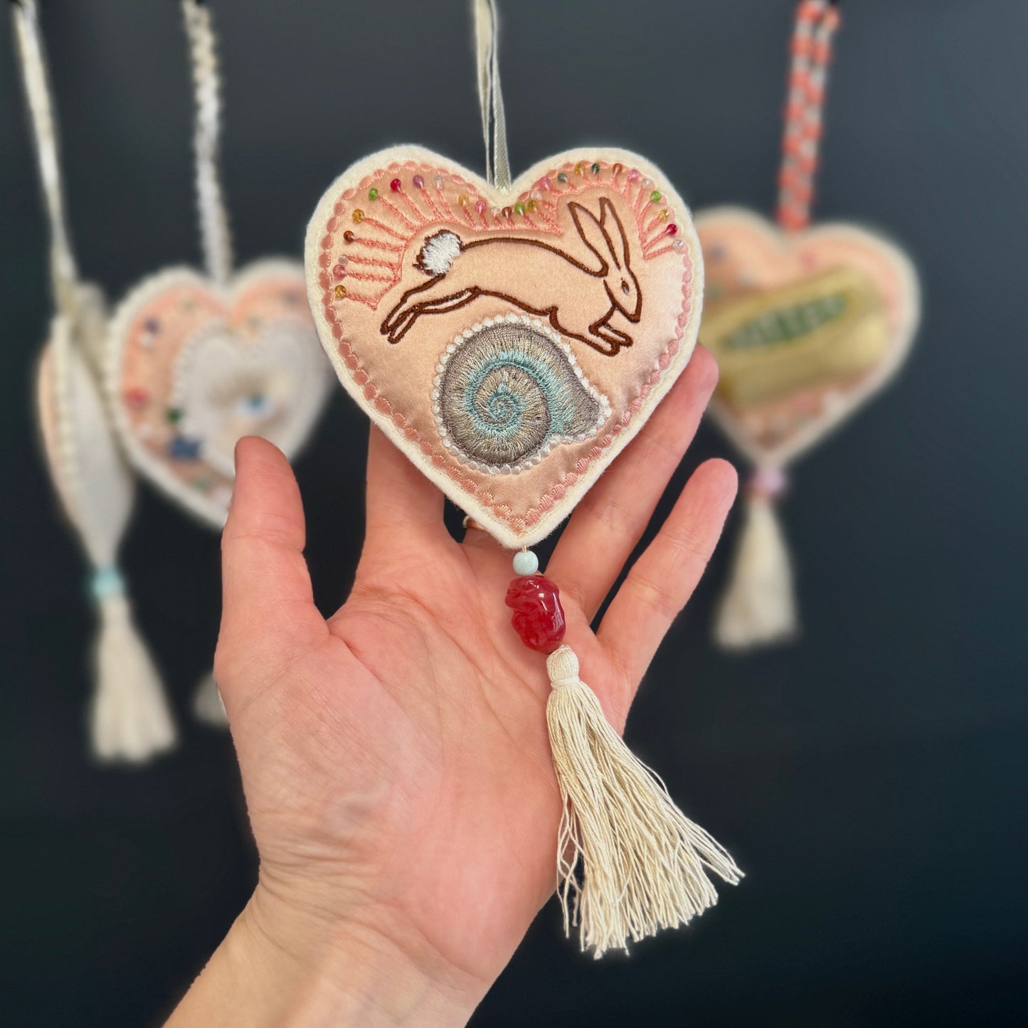 Heart-shaped embroidered ornament with a tassel held in a hand against a dark background