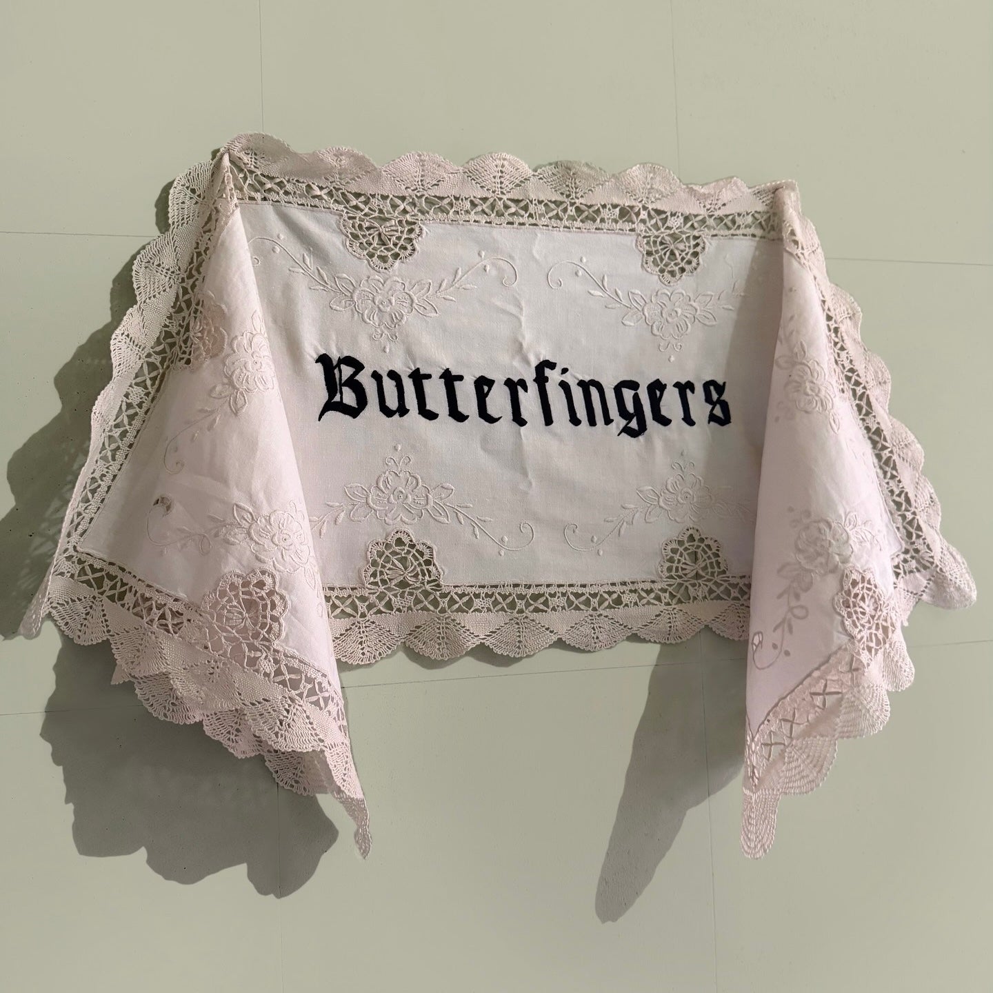 Butterfingers embroidered artwork hanging on a pale green wall