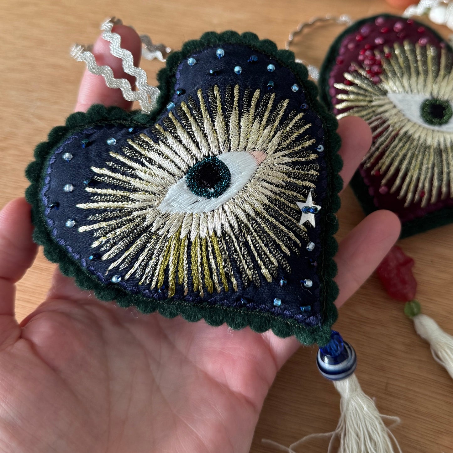 Embroidered eye-shaped heart held by a hand on a wooden surface