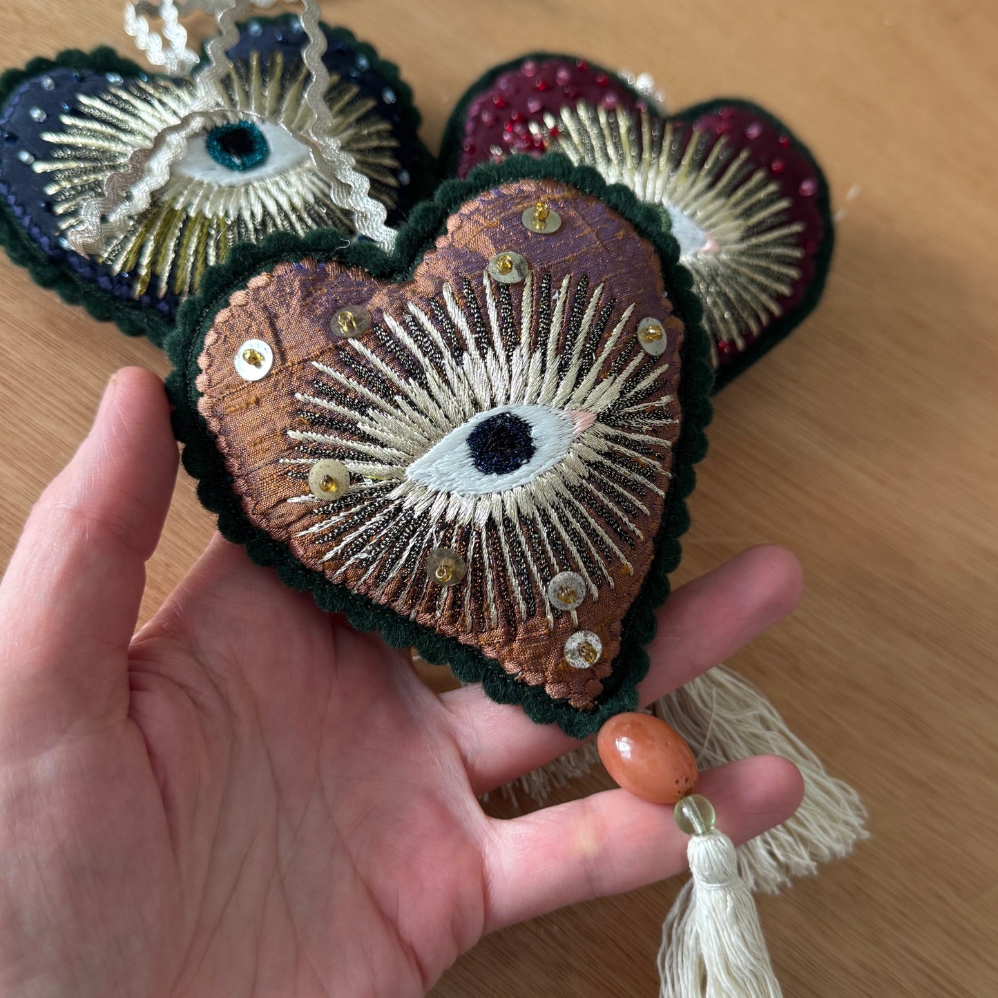 Hand holding a decorative heart-shaped ornament with eye design on a wooden surface