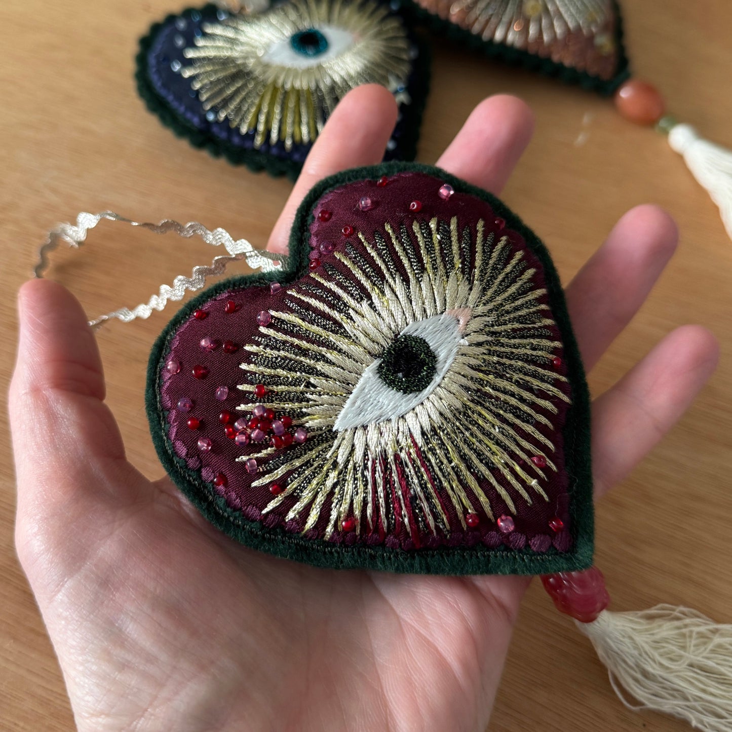 Heart-shaped embroidered patch with intricate design held in a hand on a wooden surface.