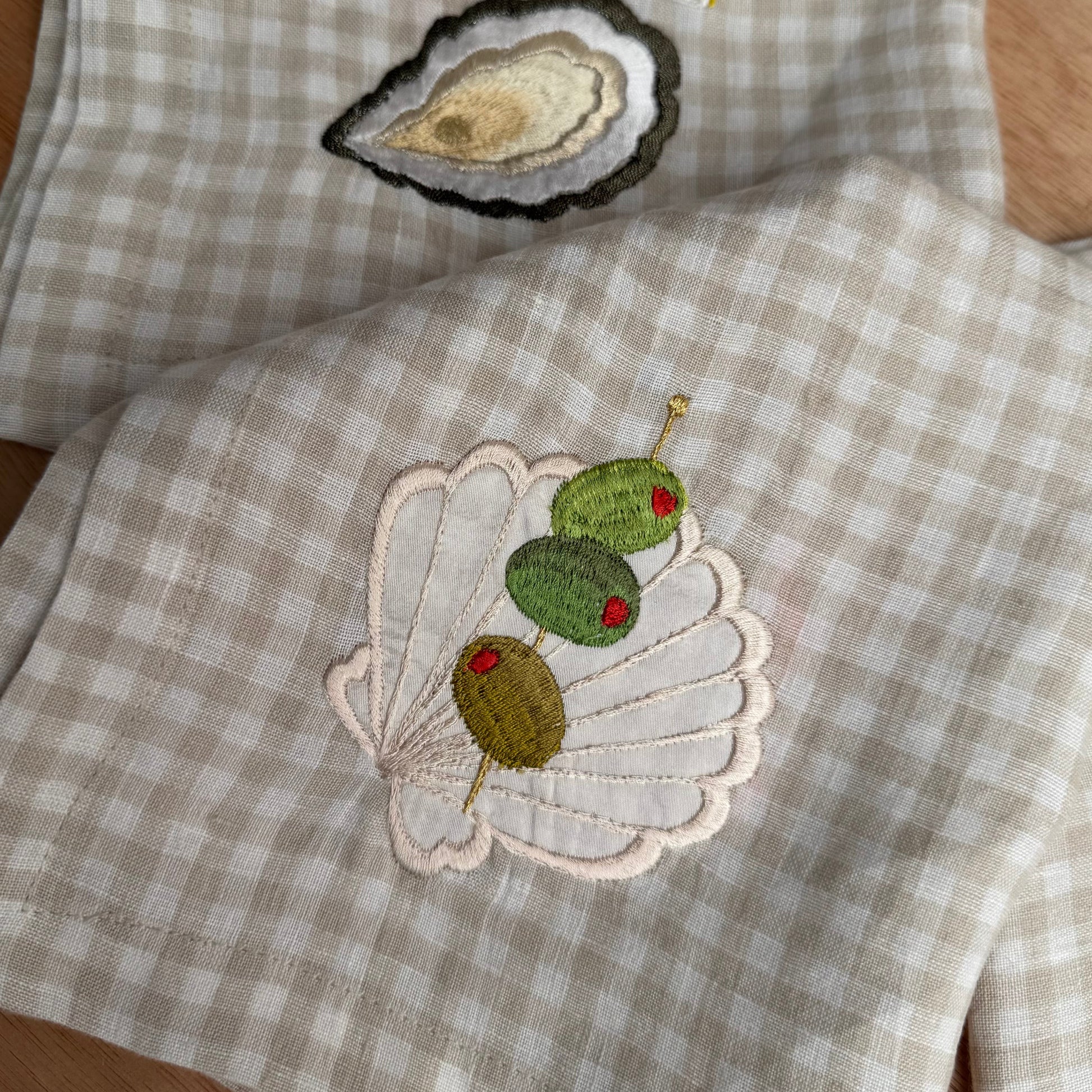 Silk shell with olive trio embroidery on gingham napkin with oyster embroidered napkin visible in the backgroud