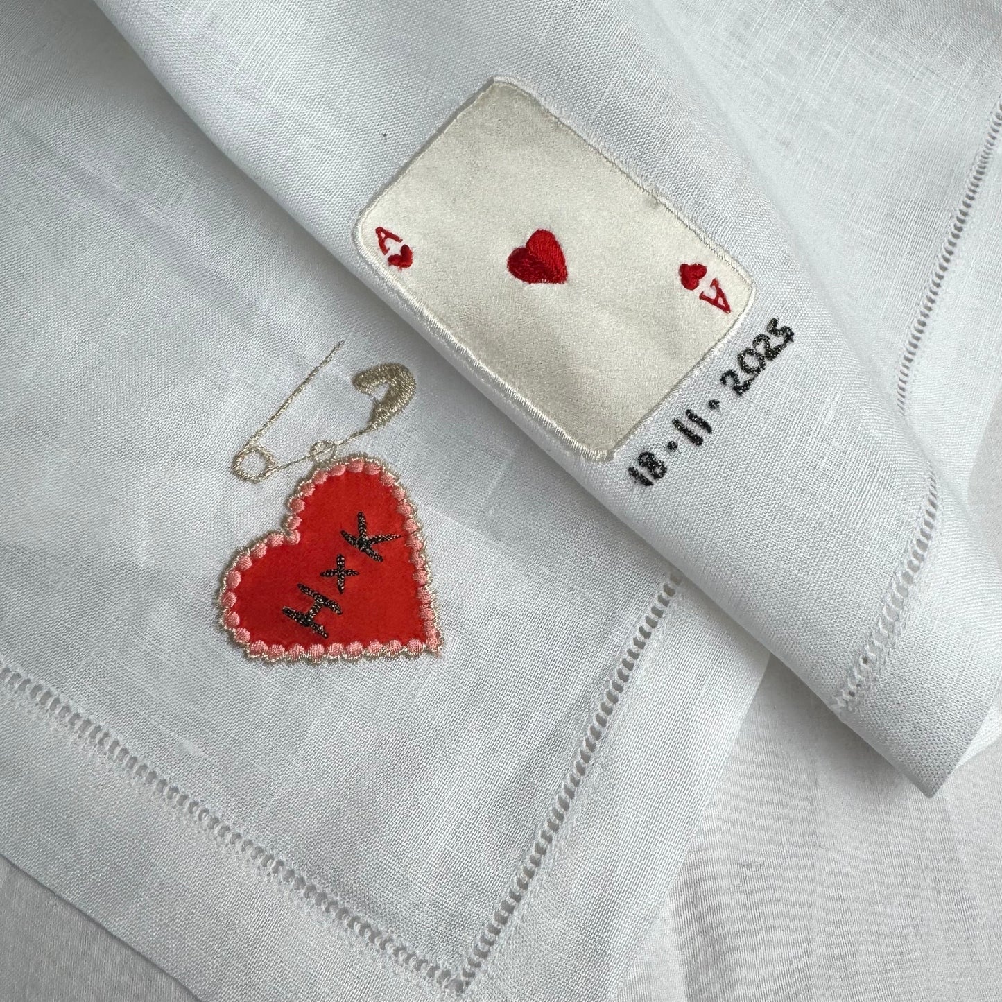 Embroidered heart charm and ace of heart playing card on a white fabric with text and dates.
