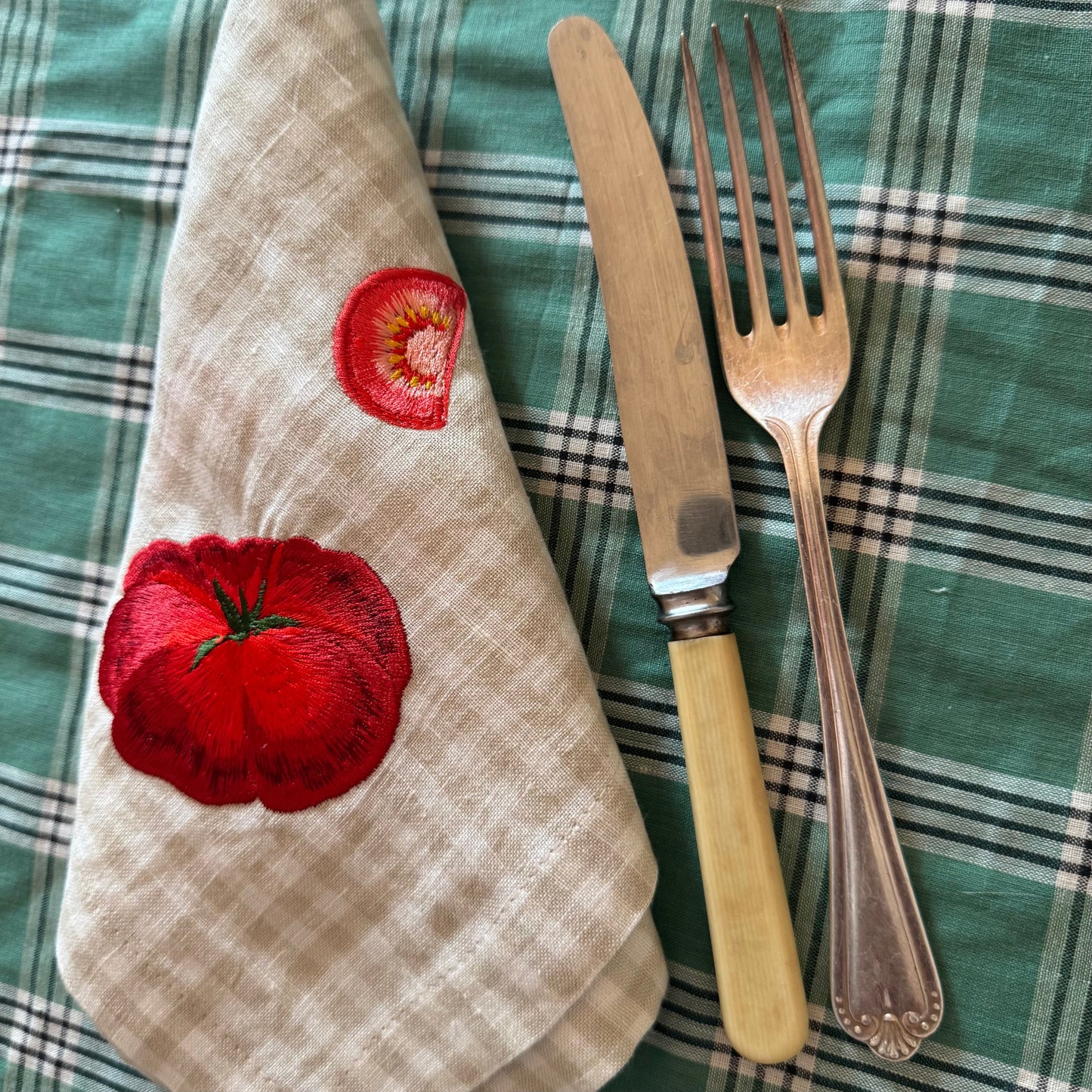 Napkin with tomato design, knife, and fork on a plaid tablecloth