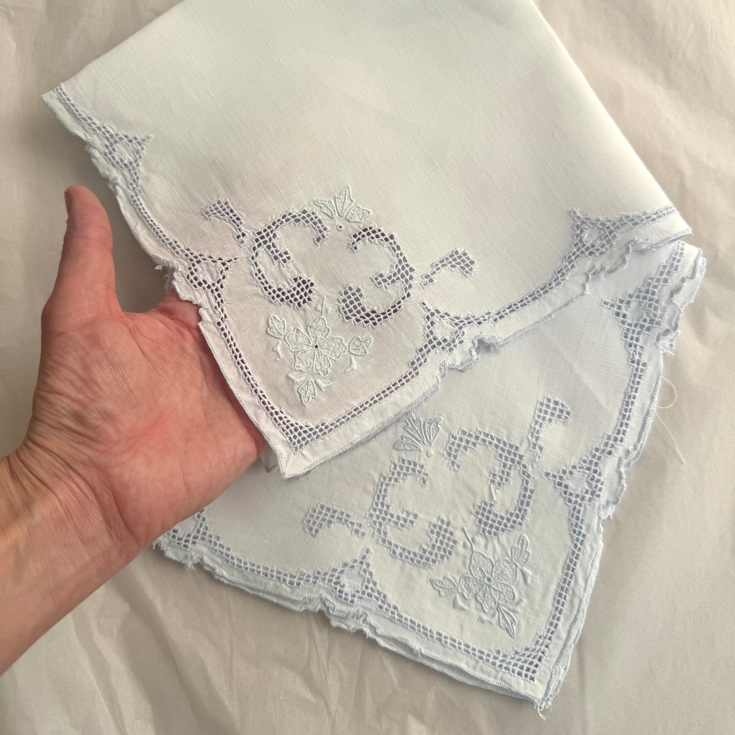 Hand holding a white embroidered handkerchief on a light background