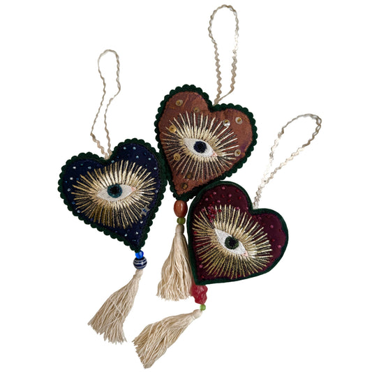 Heart-shaped decorative ornaments with eye designs and tassels on a white background