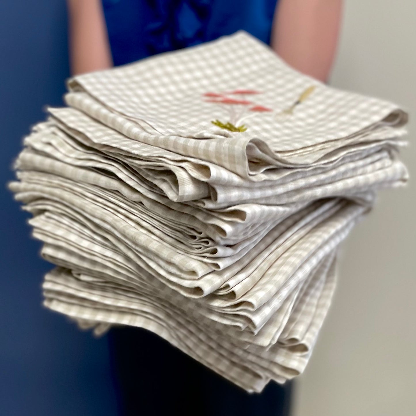 Stack of embroidered gingham napkins held in someones hands in front of a blue door