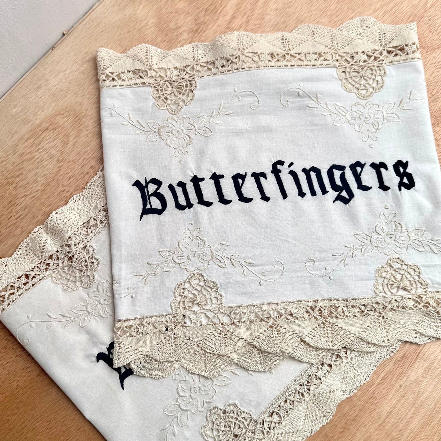 Two folded Butterfingers embroidered artworks on a wooden table