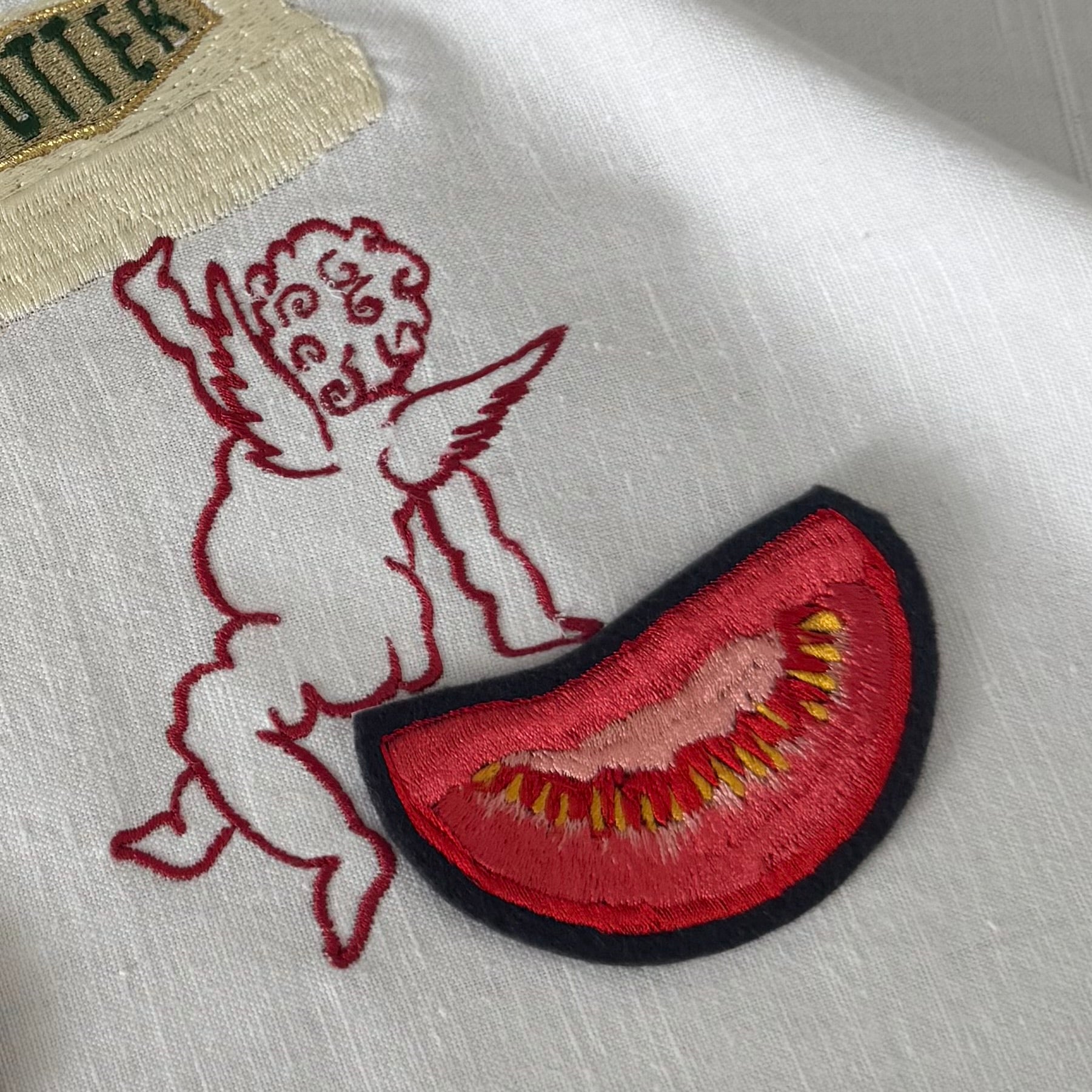 Close-up of one of the butter babies embroideries showing a red linear cherub next to a tomato slice embroidered patch