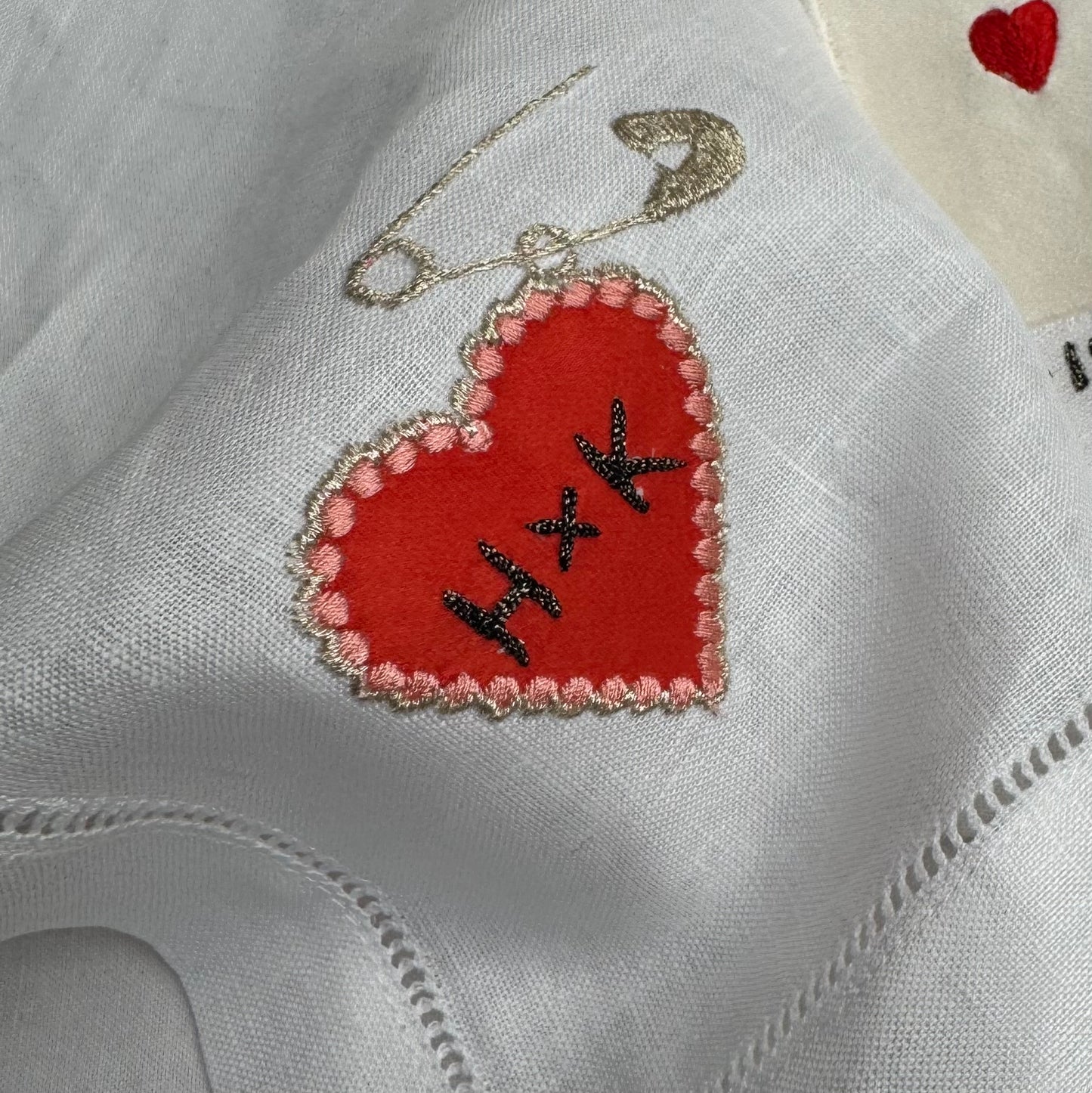 Close-up of the heart charm embroidery on the white linen fabric base of the artwork