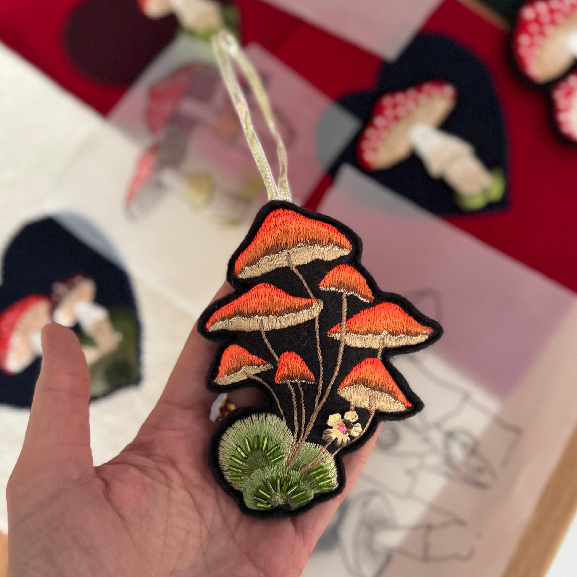 Embroidered patch of mushrooms held in a hand with a blurred background