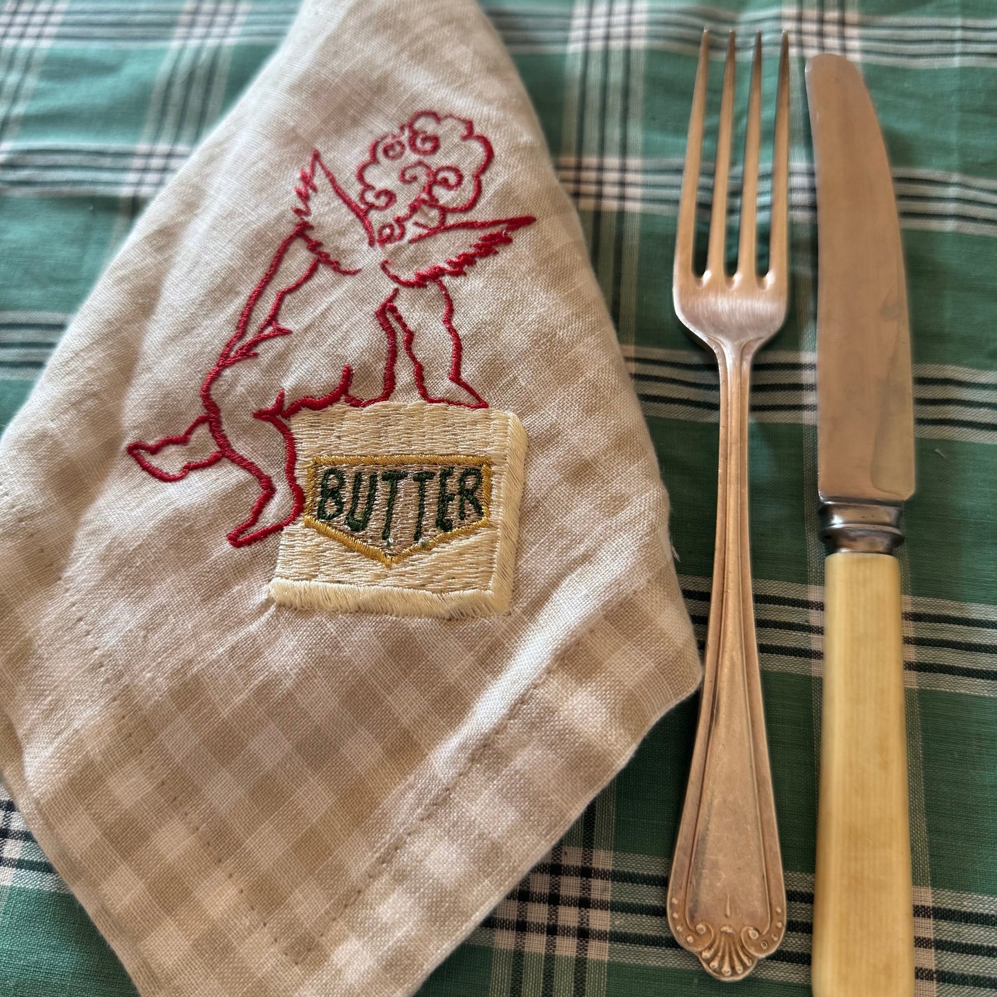 embroidered cherub and butter design on a checkered cloth with fork and knife.