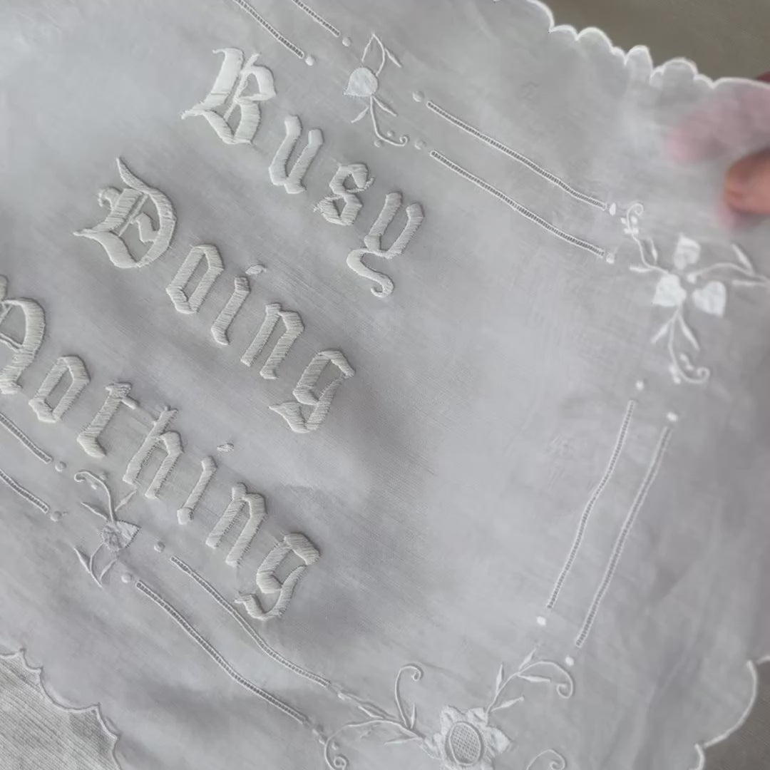 Video shows a close up of Busy Doing Nothing embroidered artwork being tilted by a hand towards the camera