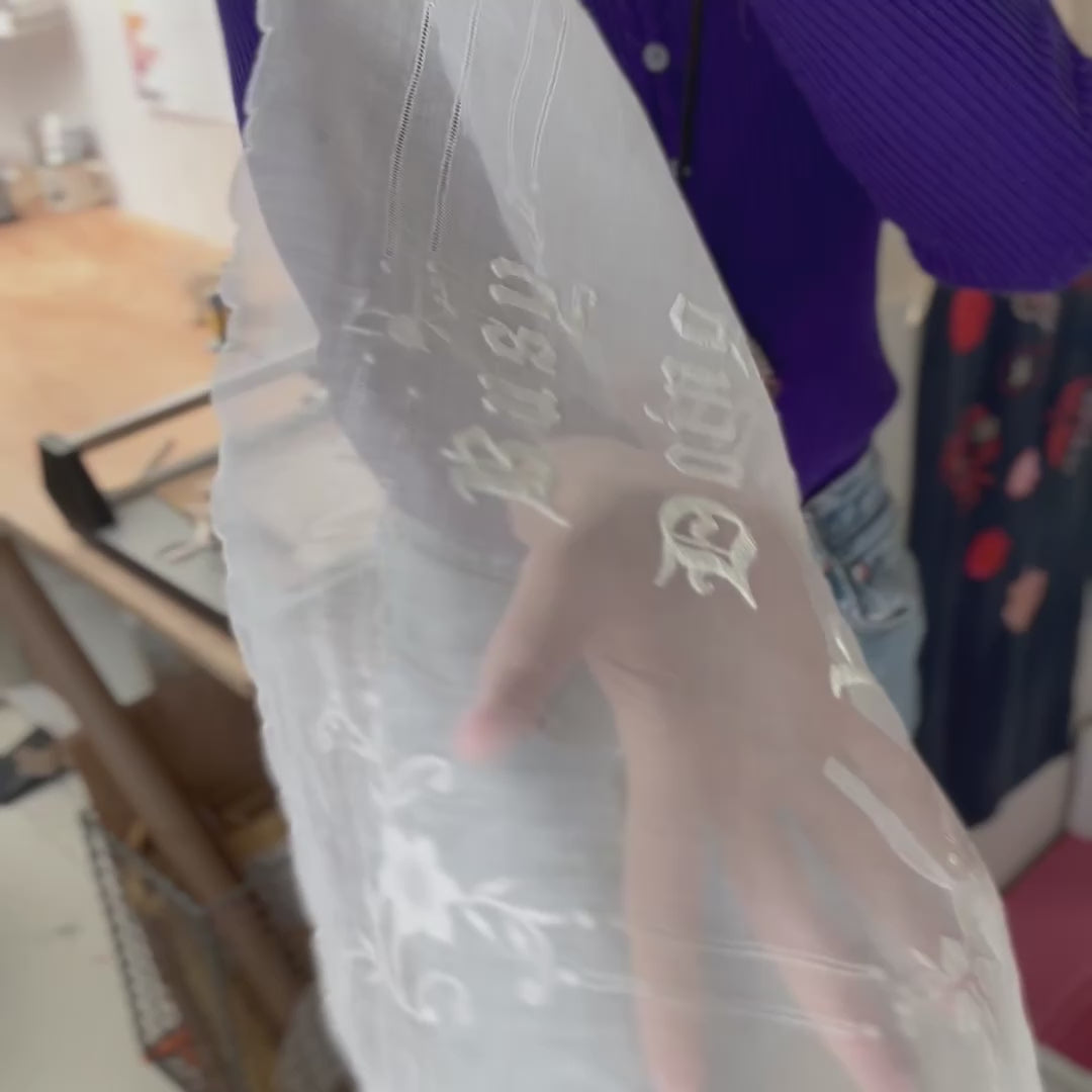 Video of a womans torso, in a purple jumper and blue jeans, tilting the Busy Doing Nothing embroidered artwork in front of their body for the camera
