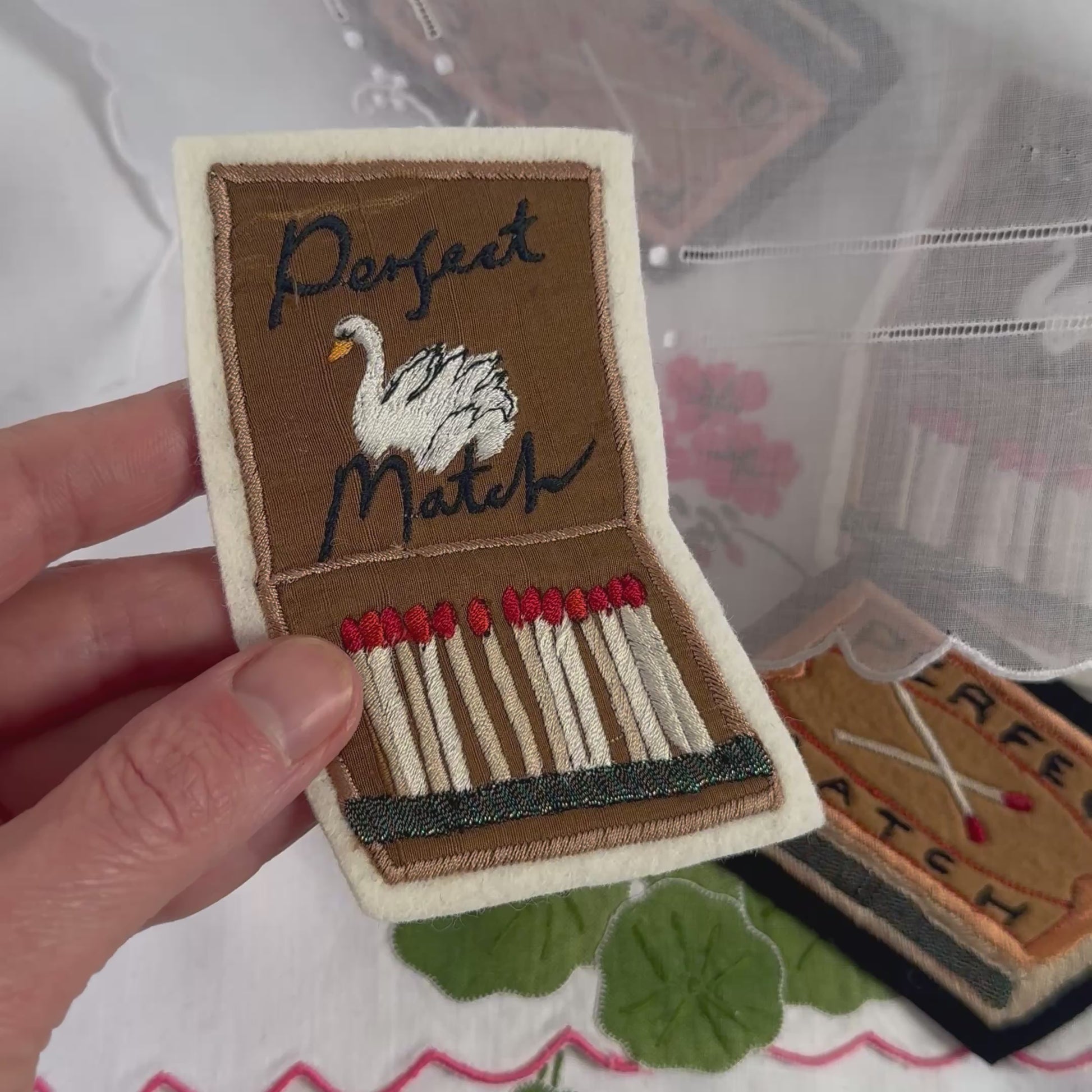 Video shows a hand holding up the embroidered matchbox and matchbook patches and bringing them closer to the screen