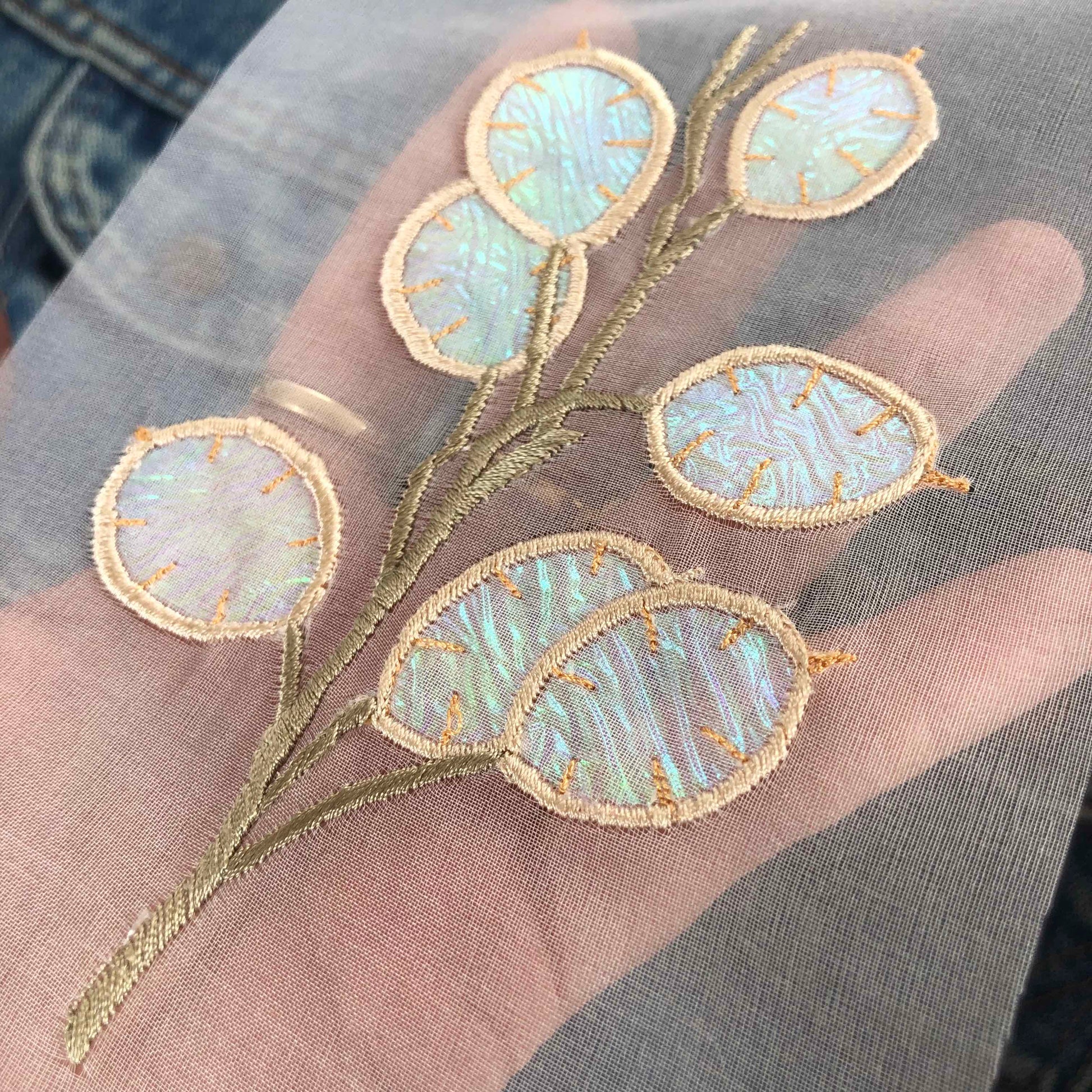 Close-up of sheer silk organza honesty embroidery with a hand visible through the embroidery