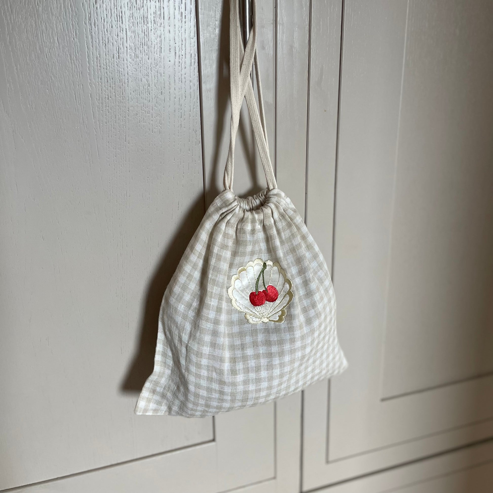 Drawstring linen bag with embroidered cherries hanging on a grey wooden cupboard door