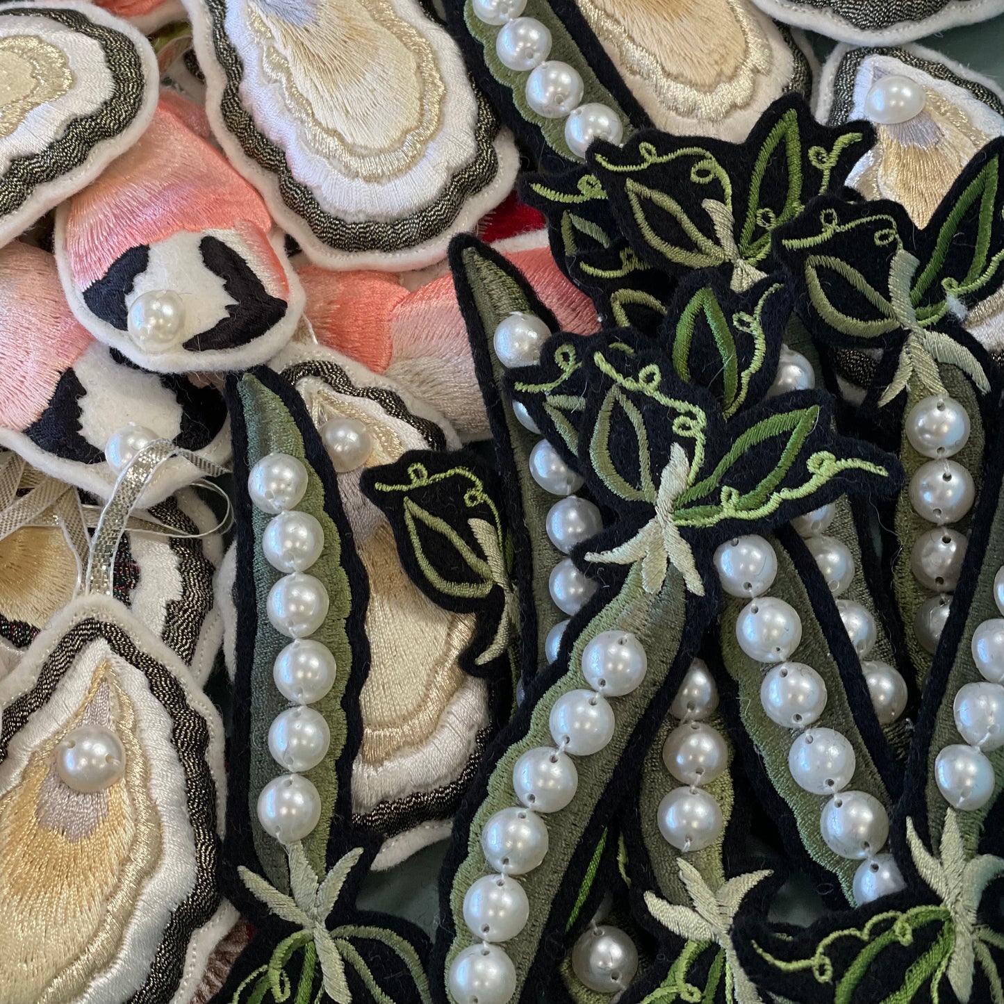A selection of Ellie Mac embroidered patches. Embroidered crab claws and oysters can be seen in the background with the embroidered peas on top