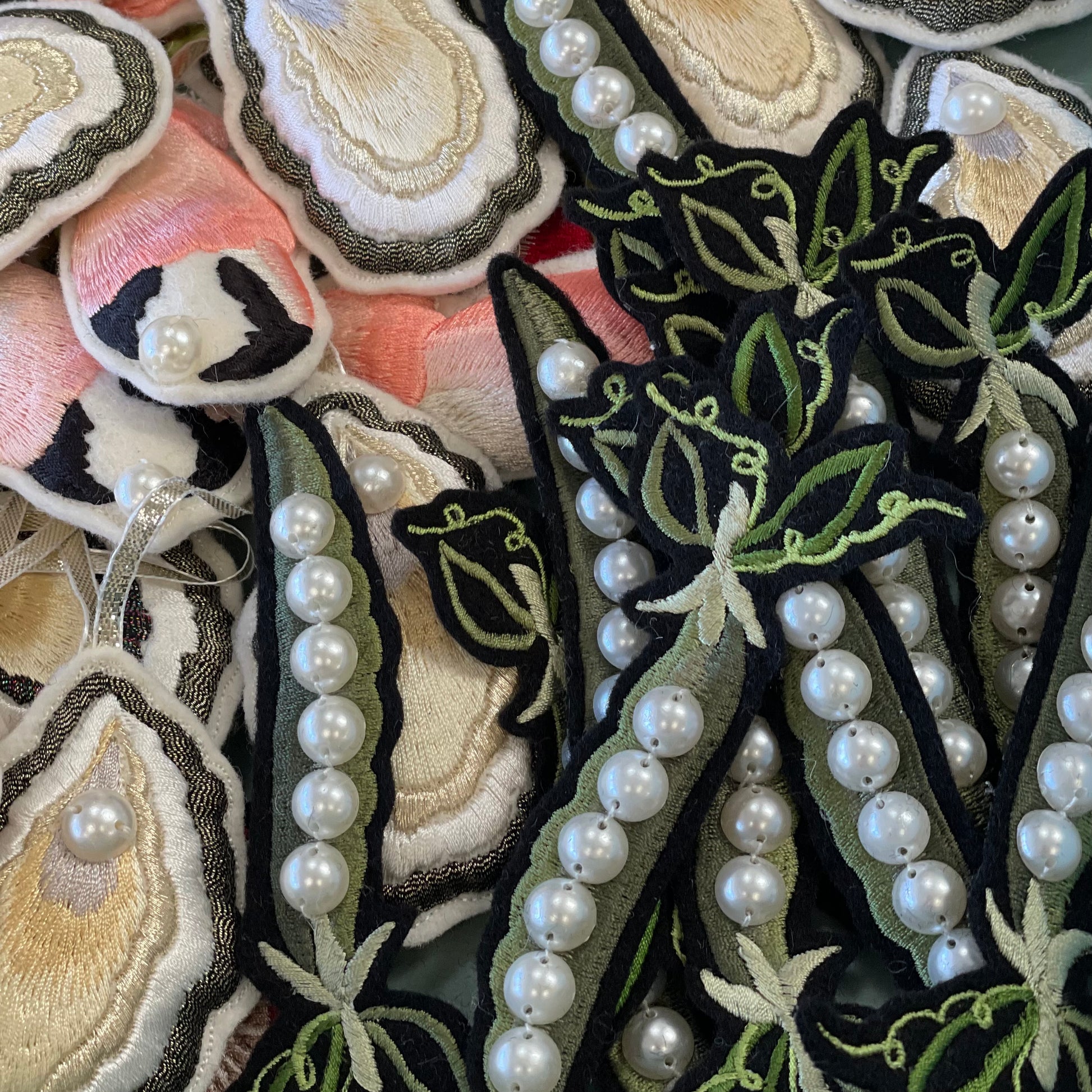 A selection of Ellie Mac embroidered patches. Embroidered crab claws and oysters can be seen in the background with the embroidered peas on top