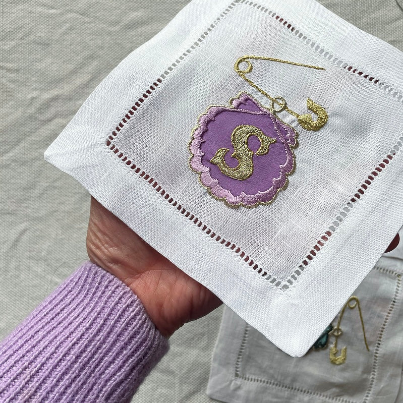 Lilac safety pin and shell artwork held in a hand over a cloth background