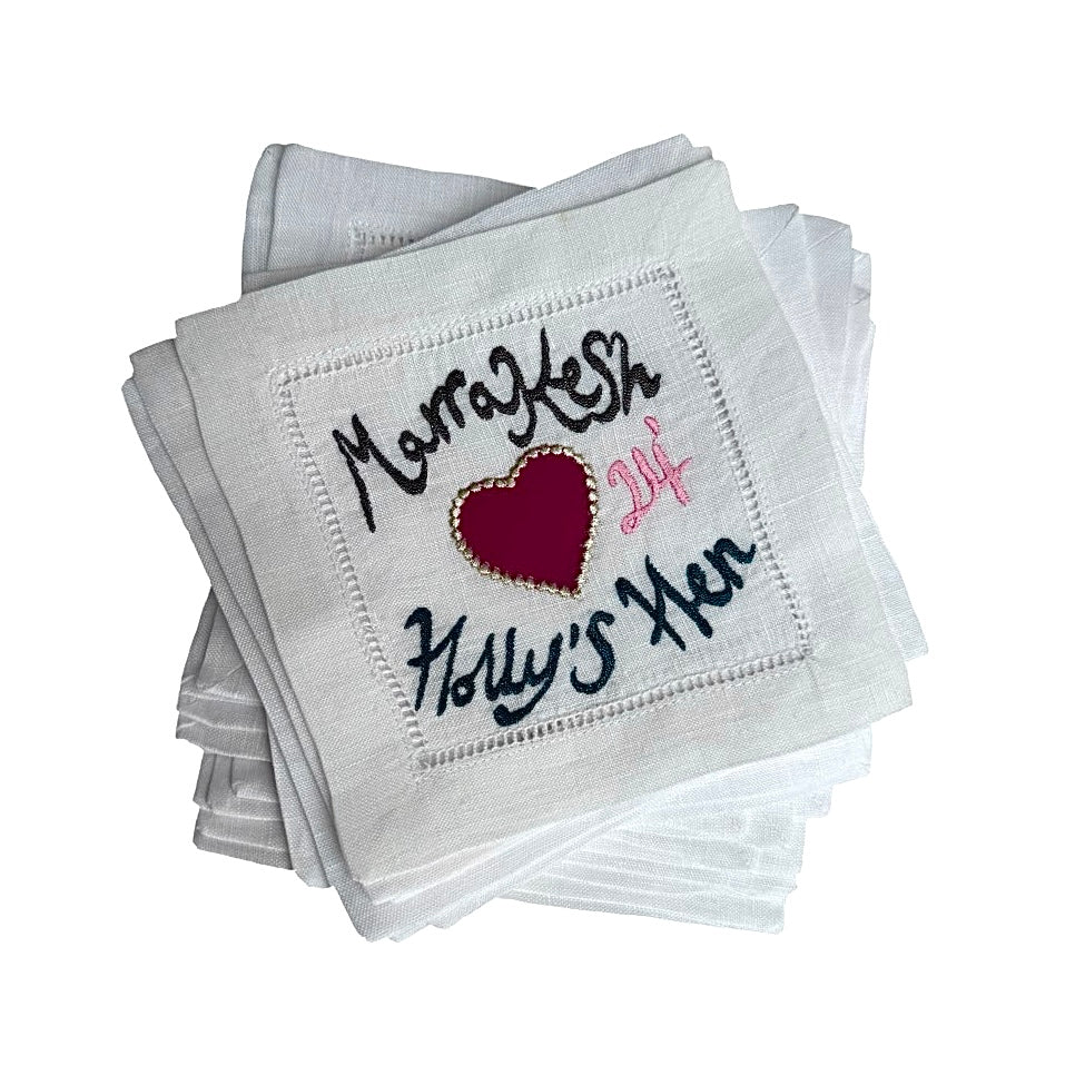 Stack of white coasters with embroidered text and a heart design on a white background