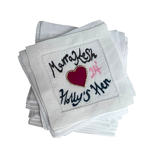 Stack of white coasters with embroidered text and a heart design on a white background