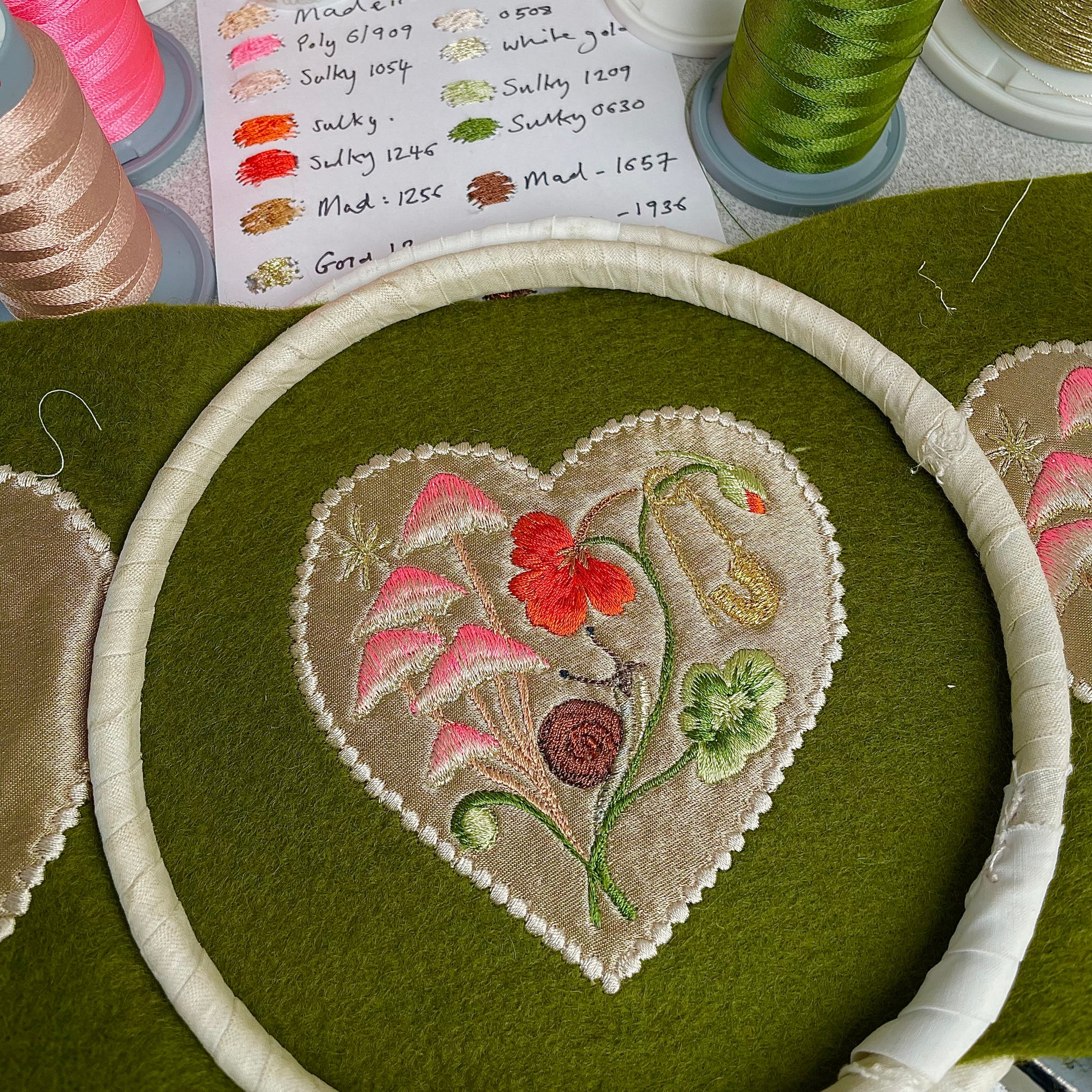 Silk applique garden embroidery seen with an embroidery machine hoop placed over the top and thread spools visible in the background