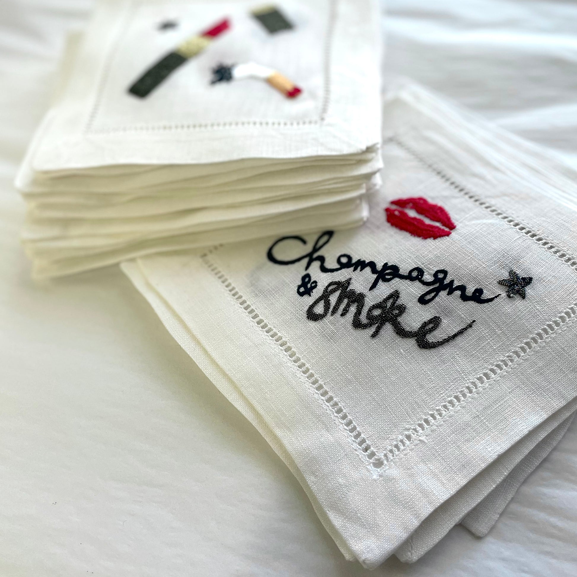 Stack of white cocktail napkins with embroidered designs on a white surface