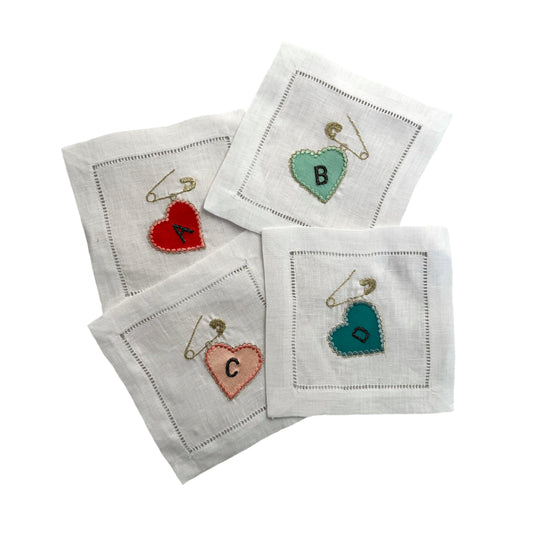 Set of four embroidered napkins with heart designs and letters on a white background