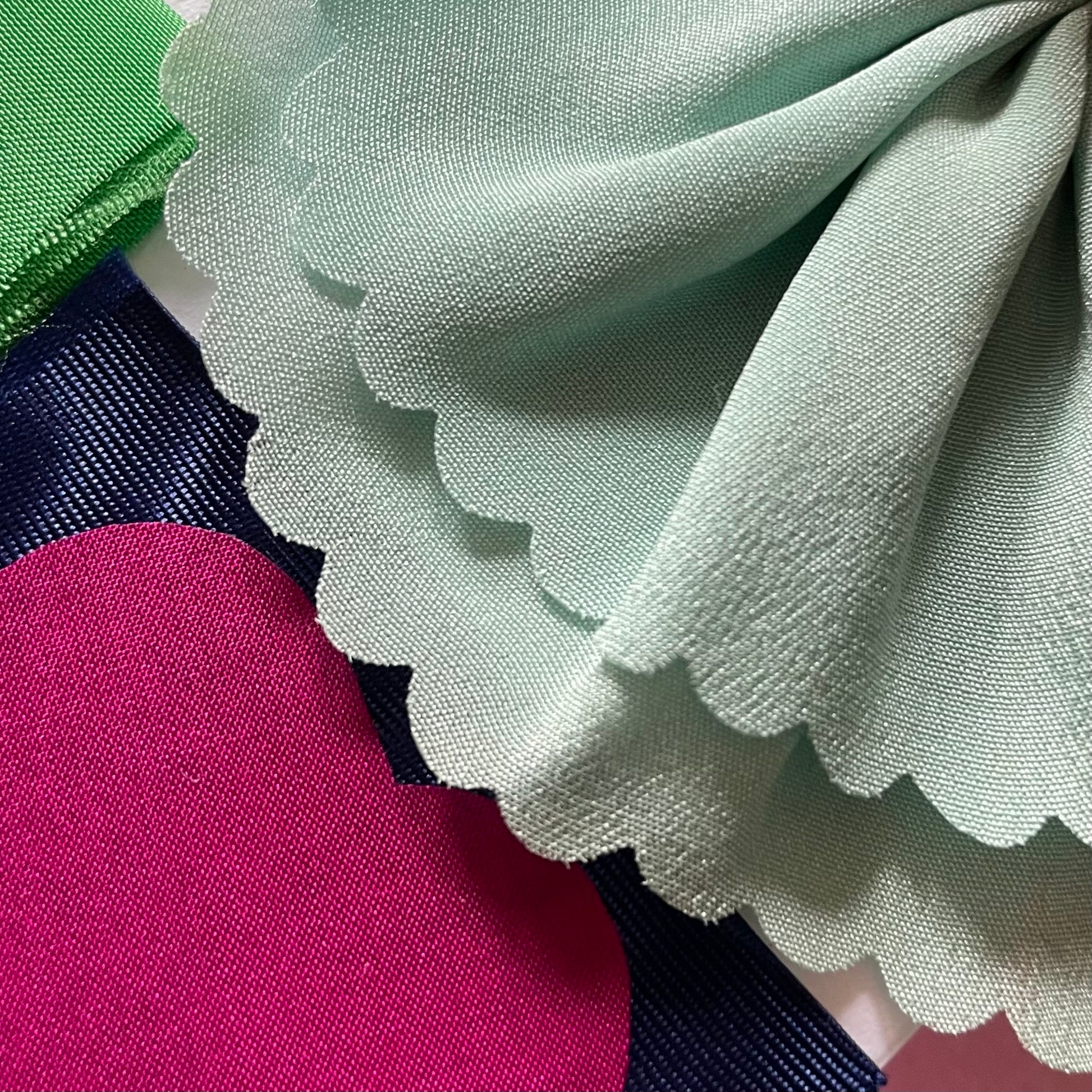 Close-up of fabrics used in the applique on the charm artworks. Lilac, hot pink, navy blue and the corner of green fabric can be seen.