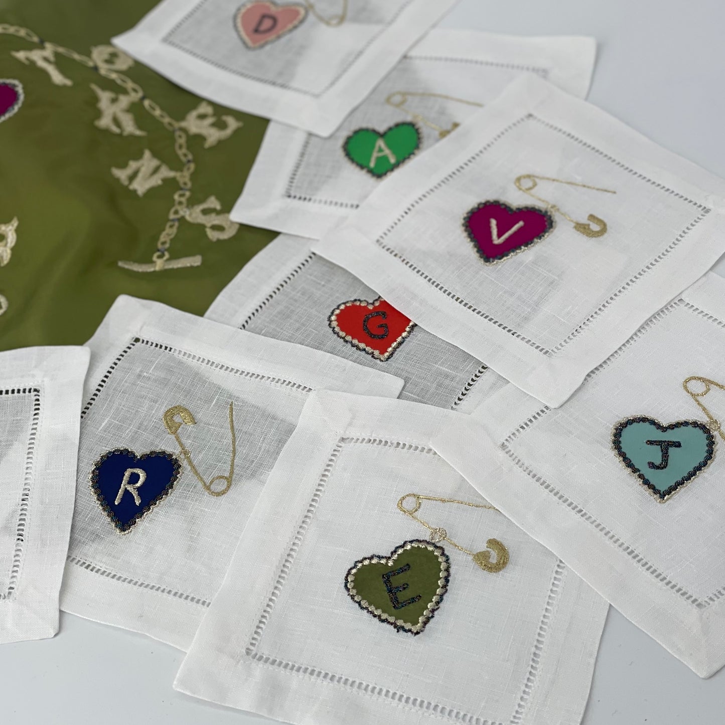 Set of embroidered heart-shaped letters on white fabric with a green fabric background.
