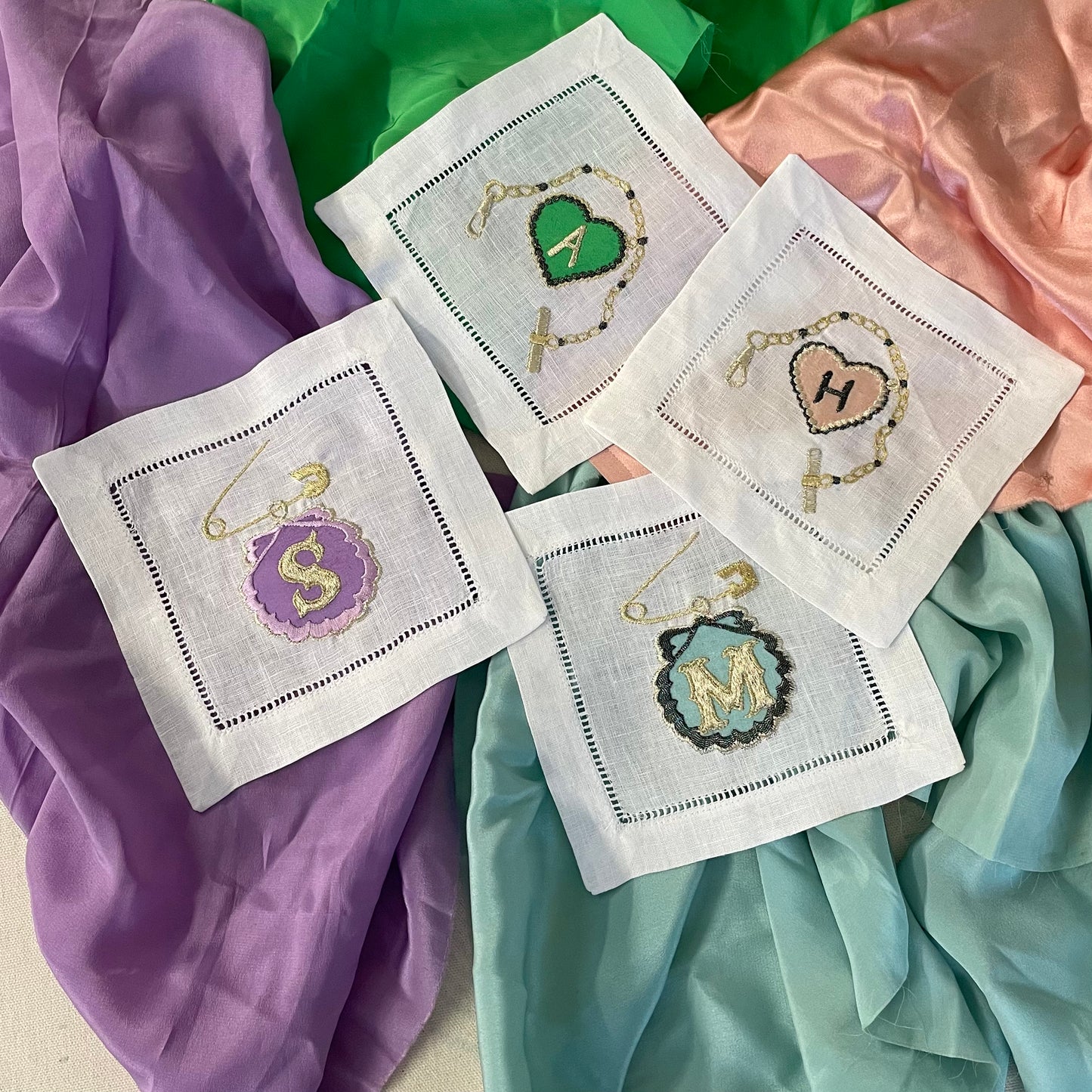 Four embroidered artworks from the Love Token collection including the custom charm bracelet and the safety pin & shell artwork
