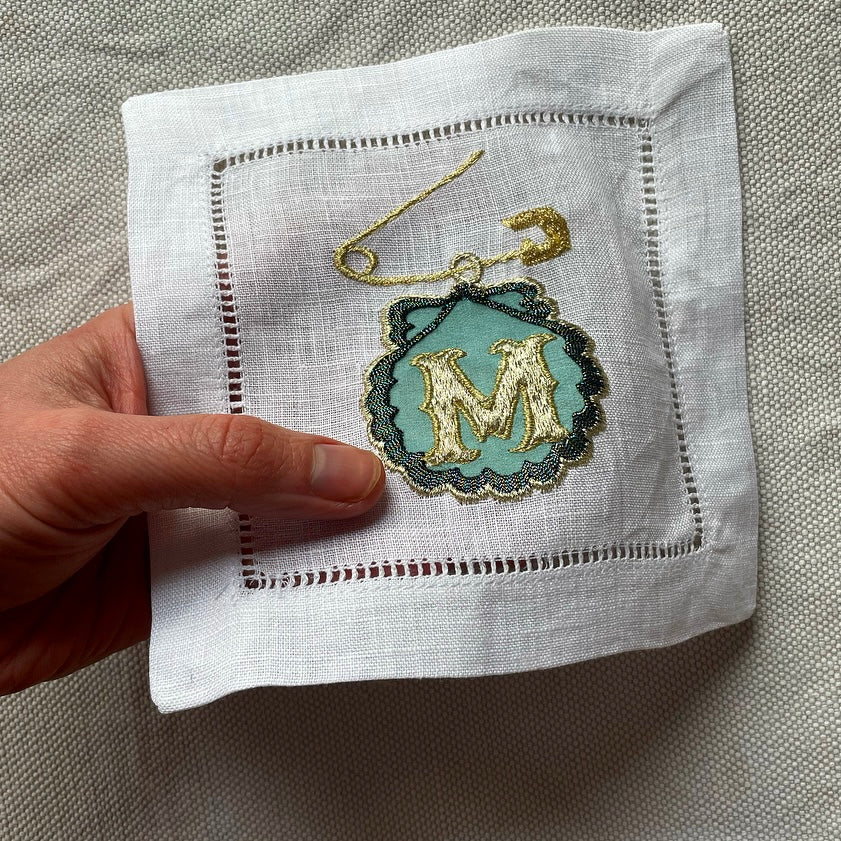 Blue safety pin and shell artwork held in a hand over a cloth background