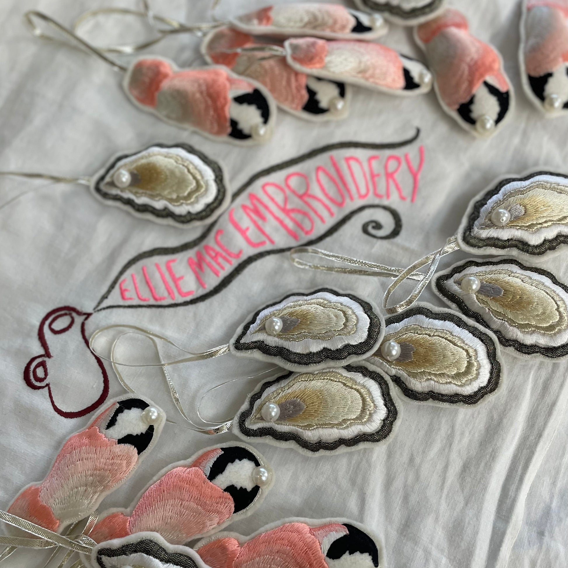White cloth with Ellie Mac Embroidery sewn on and a selection of embroidered decorations of oysters and crab claws laid on top