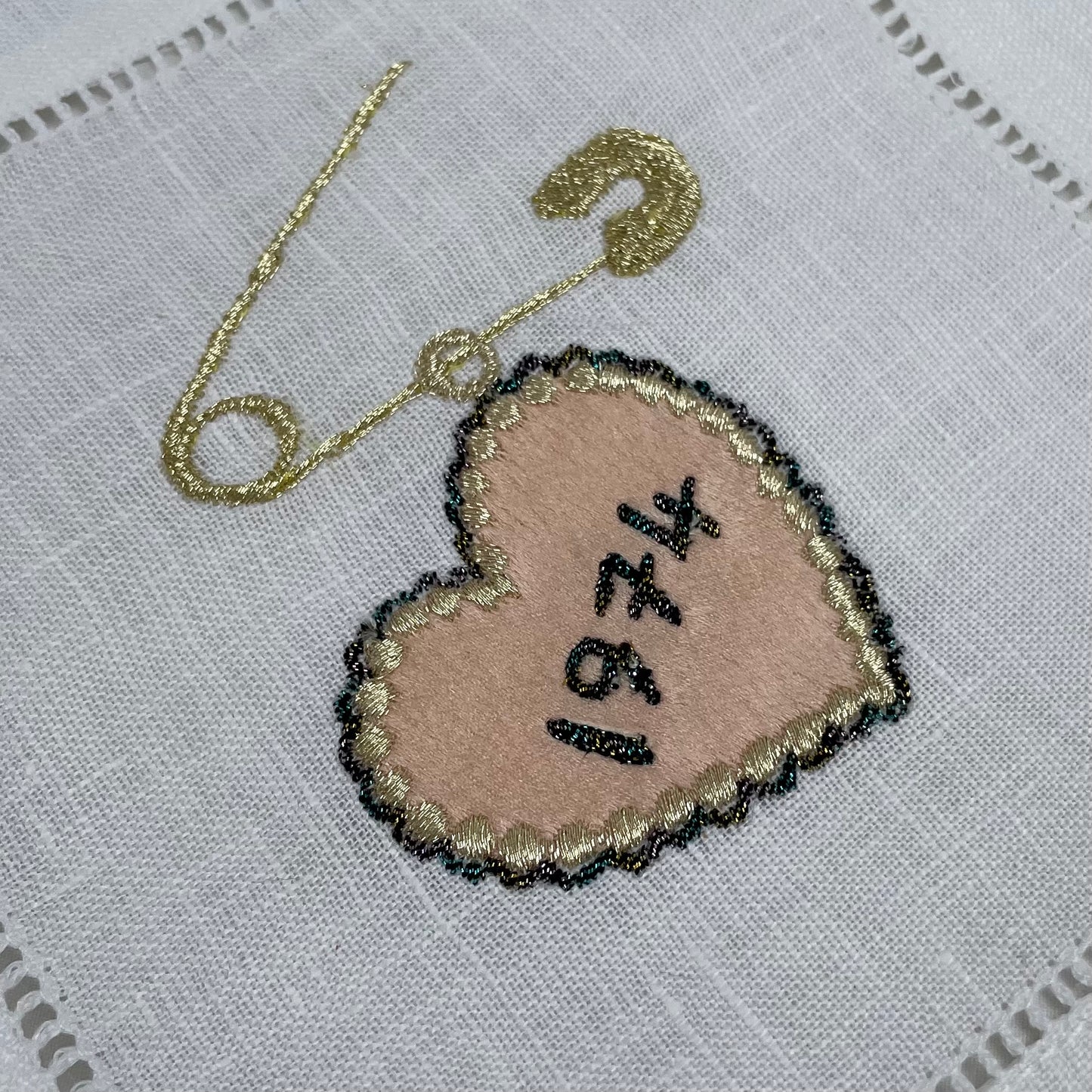 Close-up of embroidered date heart and pin charm in peach