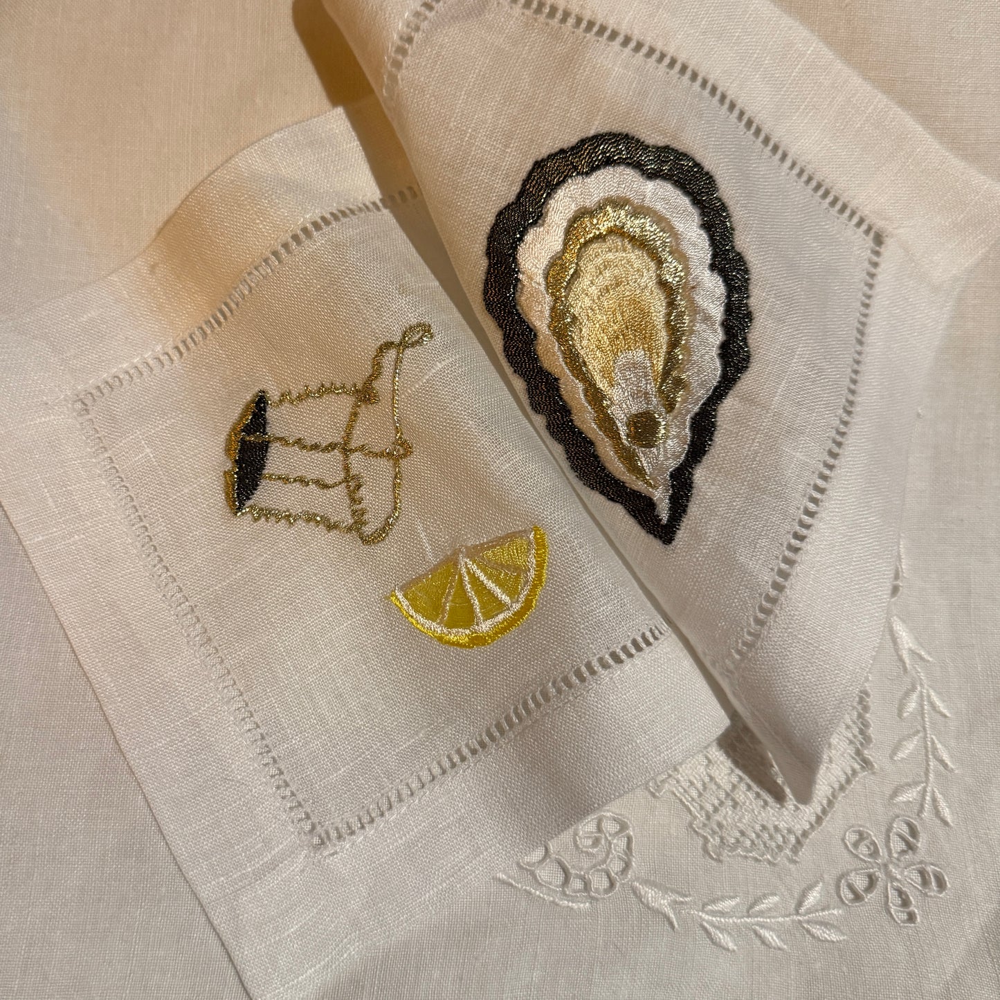 Embroidered napkins with oyster, champagne muselet and lemon design on white fabric.