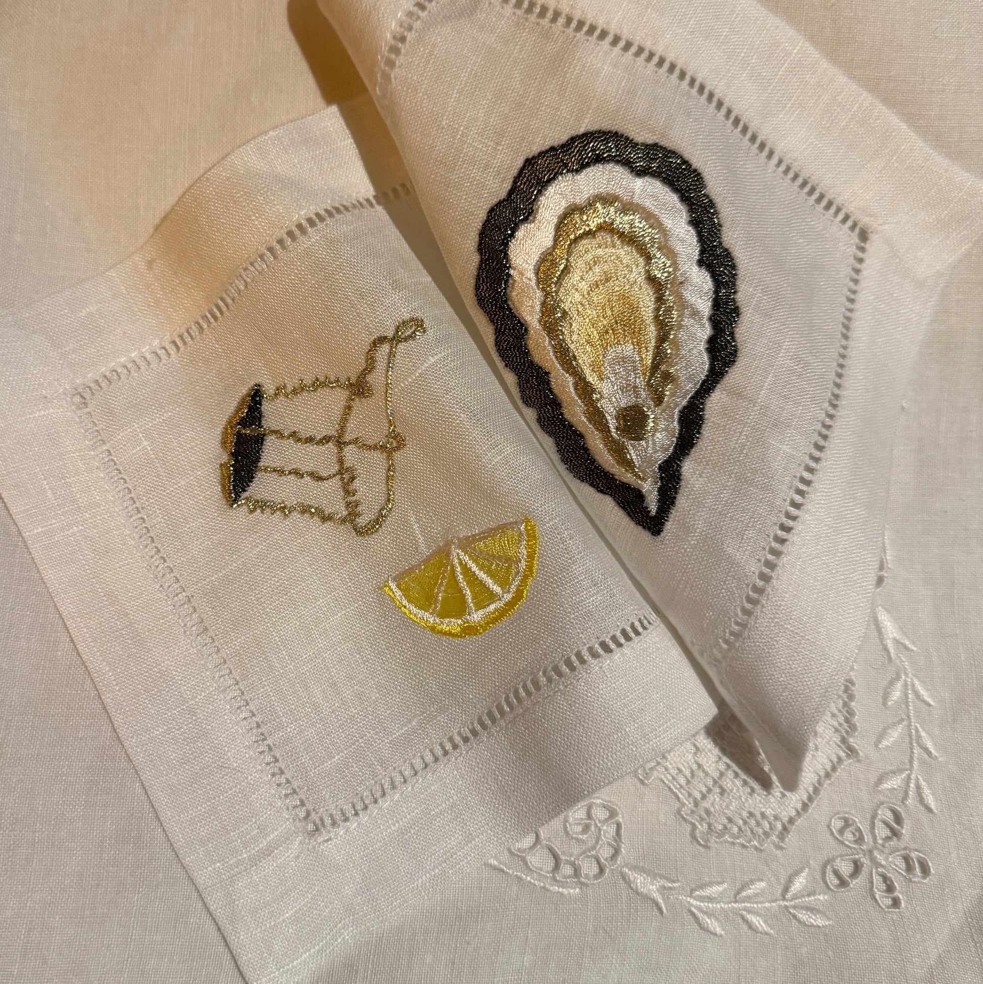 Embroidered napkins with oyster, champagne muselet and lemon design on white fabric.