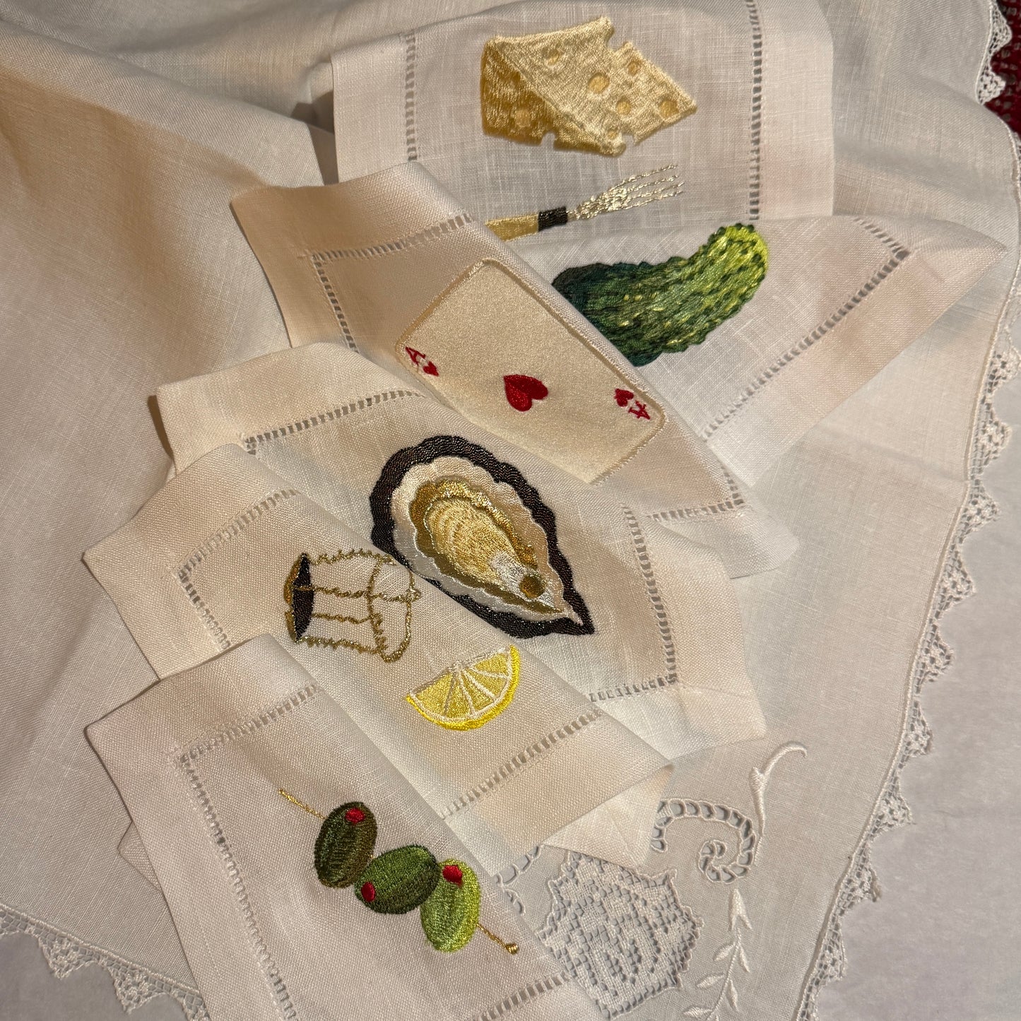 Embroidered linen napkins with cocktail party themed designs on a textured fabric background.
