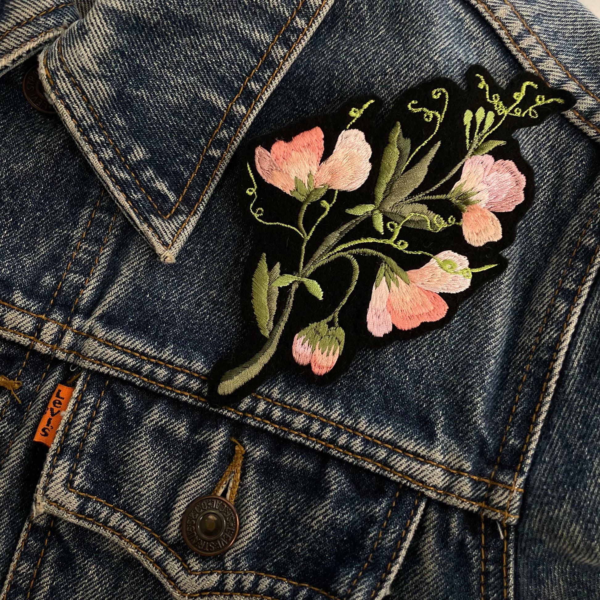 Embroidered sweet pea patch seen on the front shoulder of a blue denim jacket
