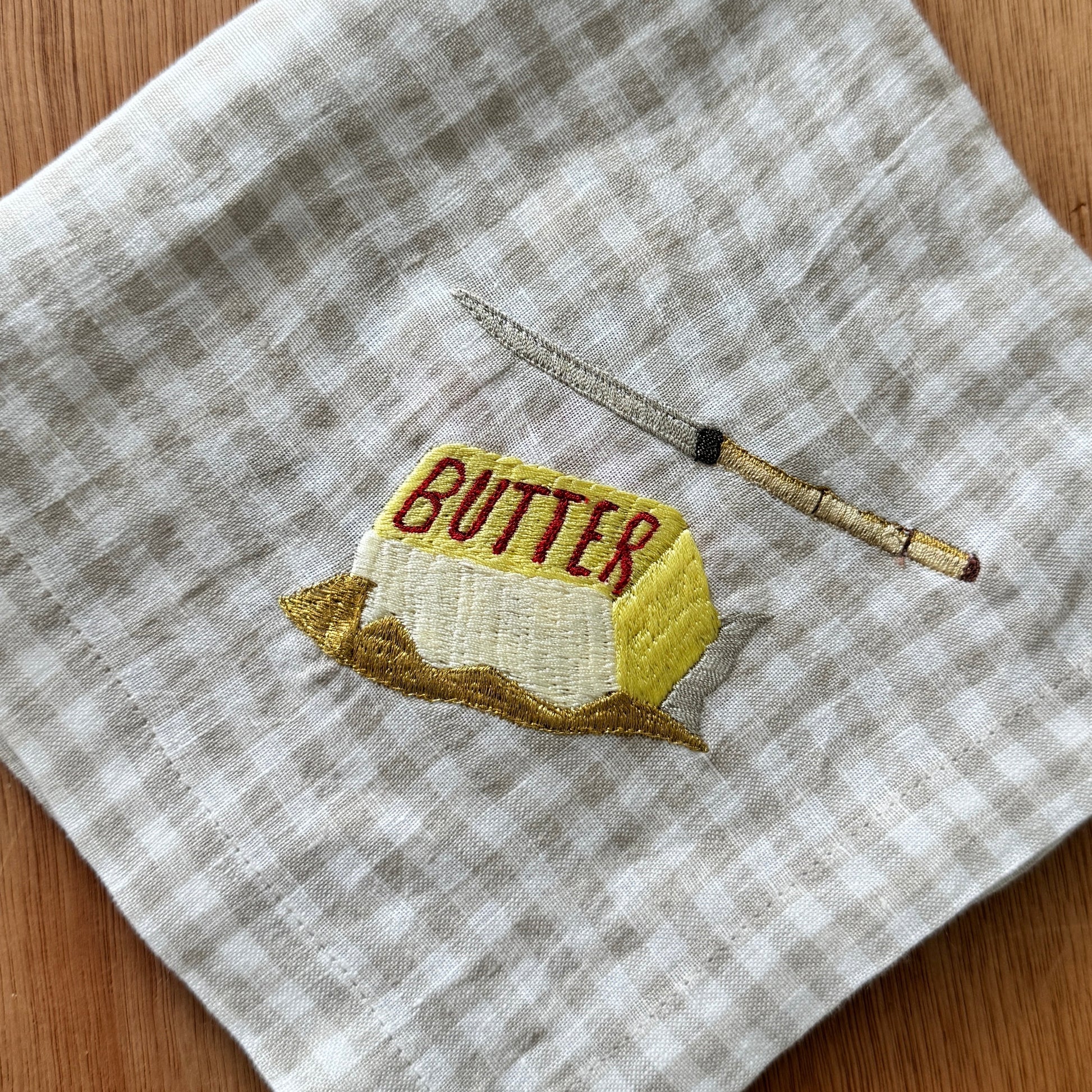Embroidered butter block and knife on a checkered fabric background