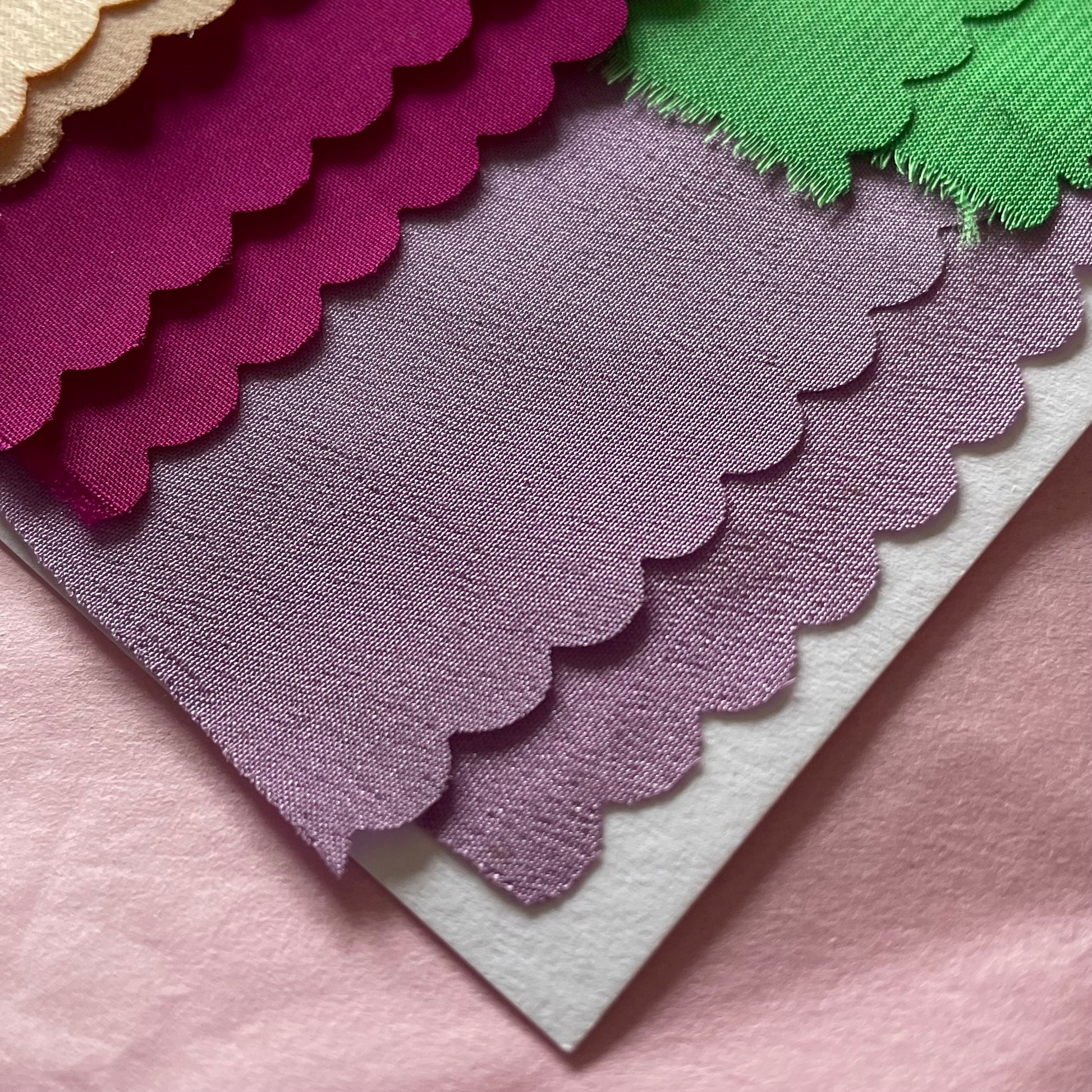 Close-up of fabrics used in the applique on the charm artworks. Lilac, hot pink and the corner of peach are seen. 