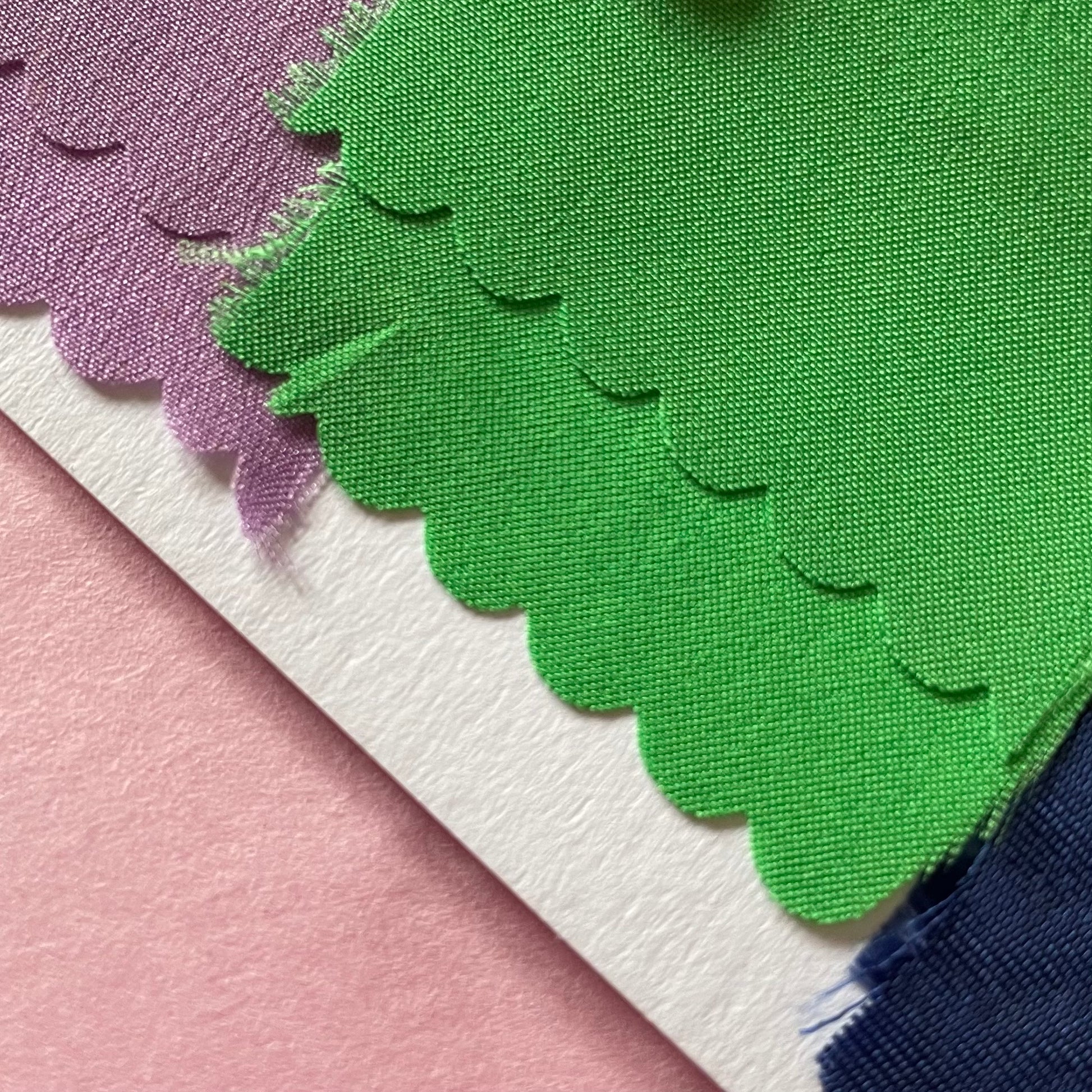 Close-up of fabrics used in the applique on the charm artworks. Lilac, green and the corner of navy blue fabric can be seen.