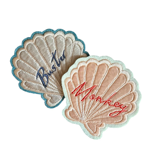 Silk applique shell patches, one with blue embroidered writing that says 'Buster' and one with pink embroidered writing that says 'Monkey' 