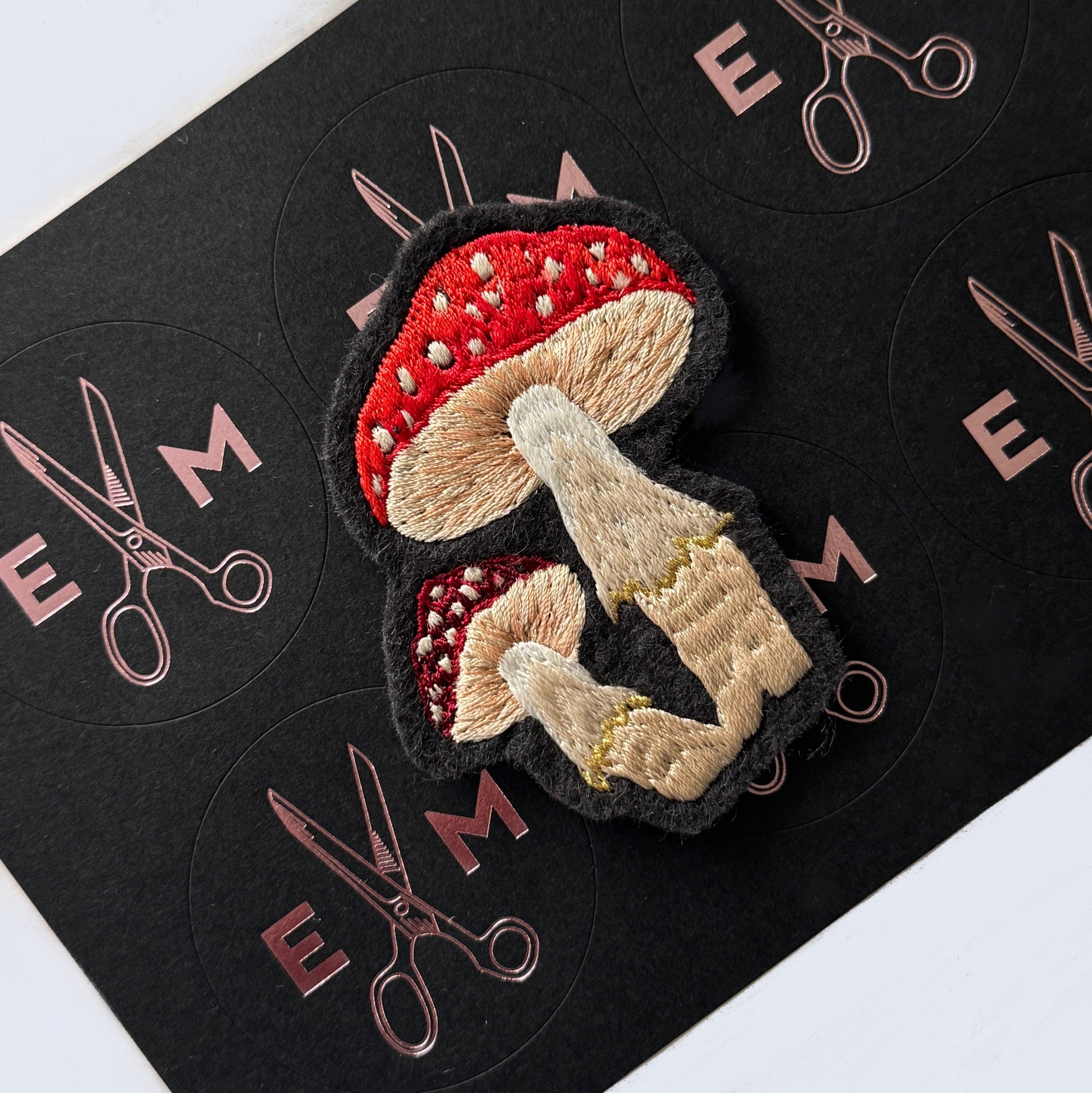 Embroidered patch of mushrooms on a black background with scissors design.
