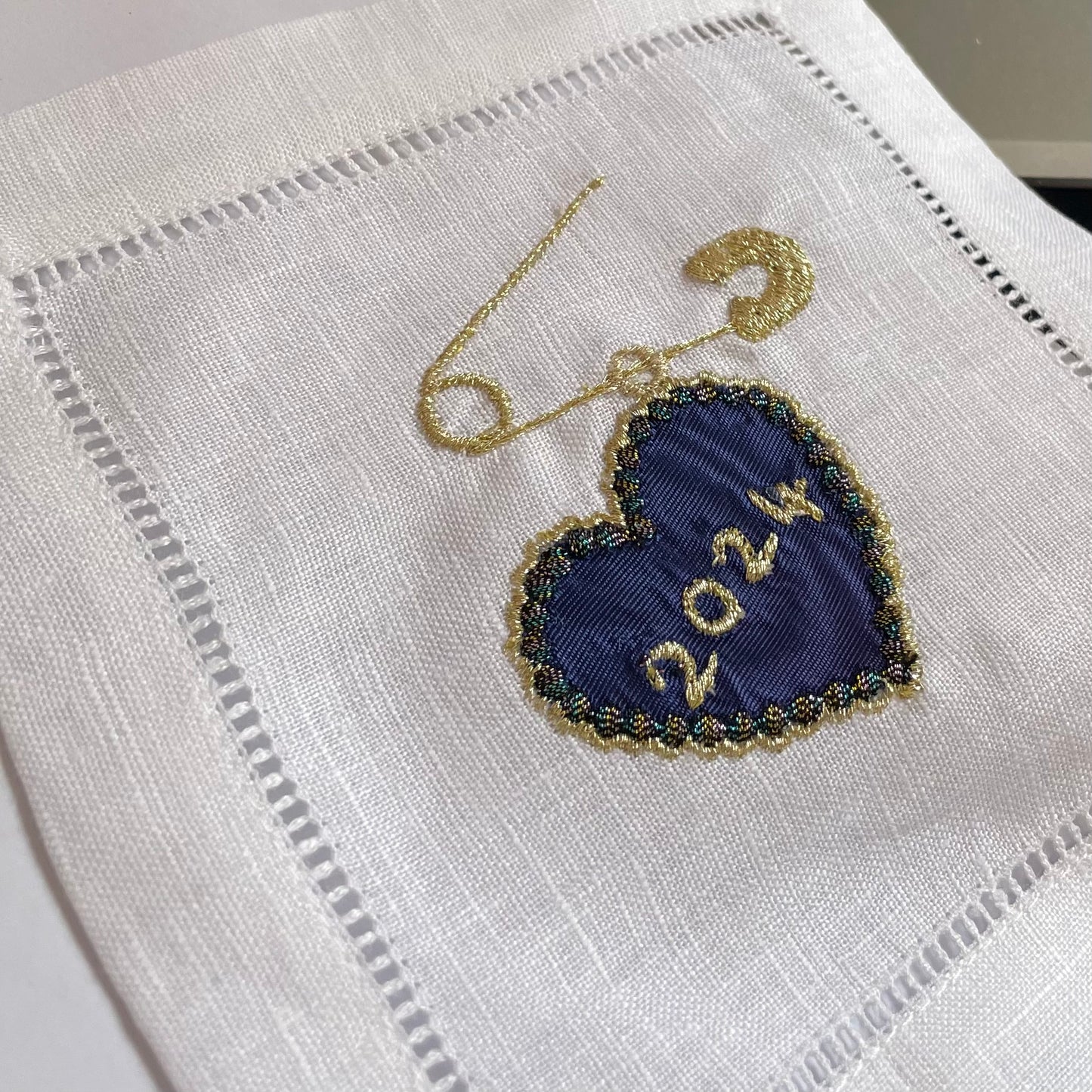 Close-up of embroidered date heart and pin charm in navy blue