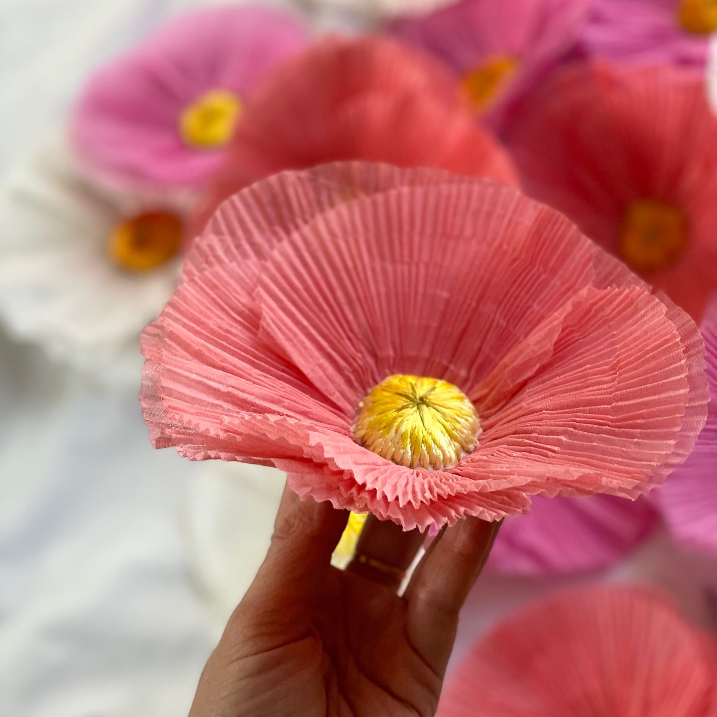 A pink version of the pleated fried egg flower embroidery held in a hand