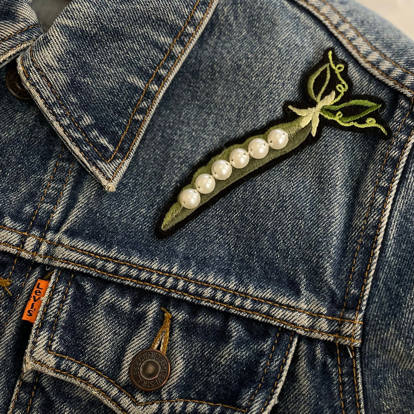 Single pea and pearl embroidered patch shown on the top front shoulder of a denim jacket